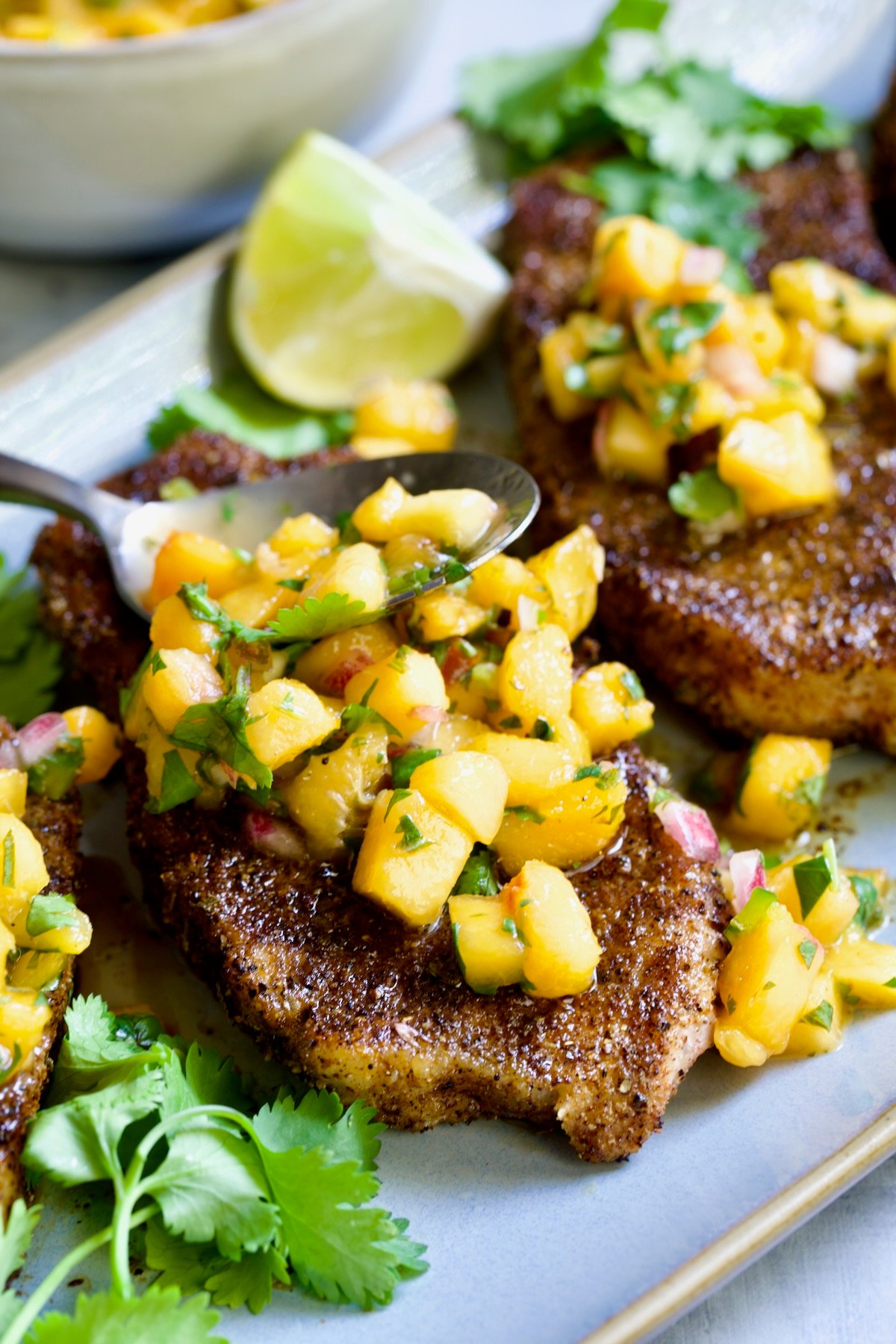 Pork Chops with Peach Salsa on oval gray platter with salsa-filled spoon resting on one of the chops.