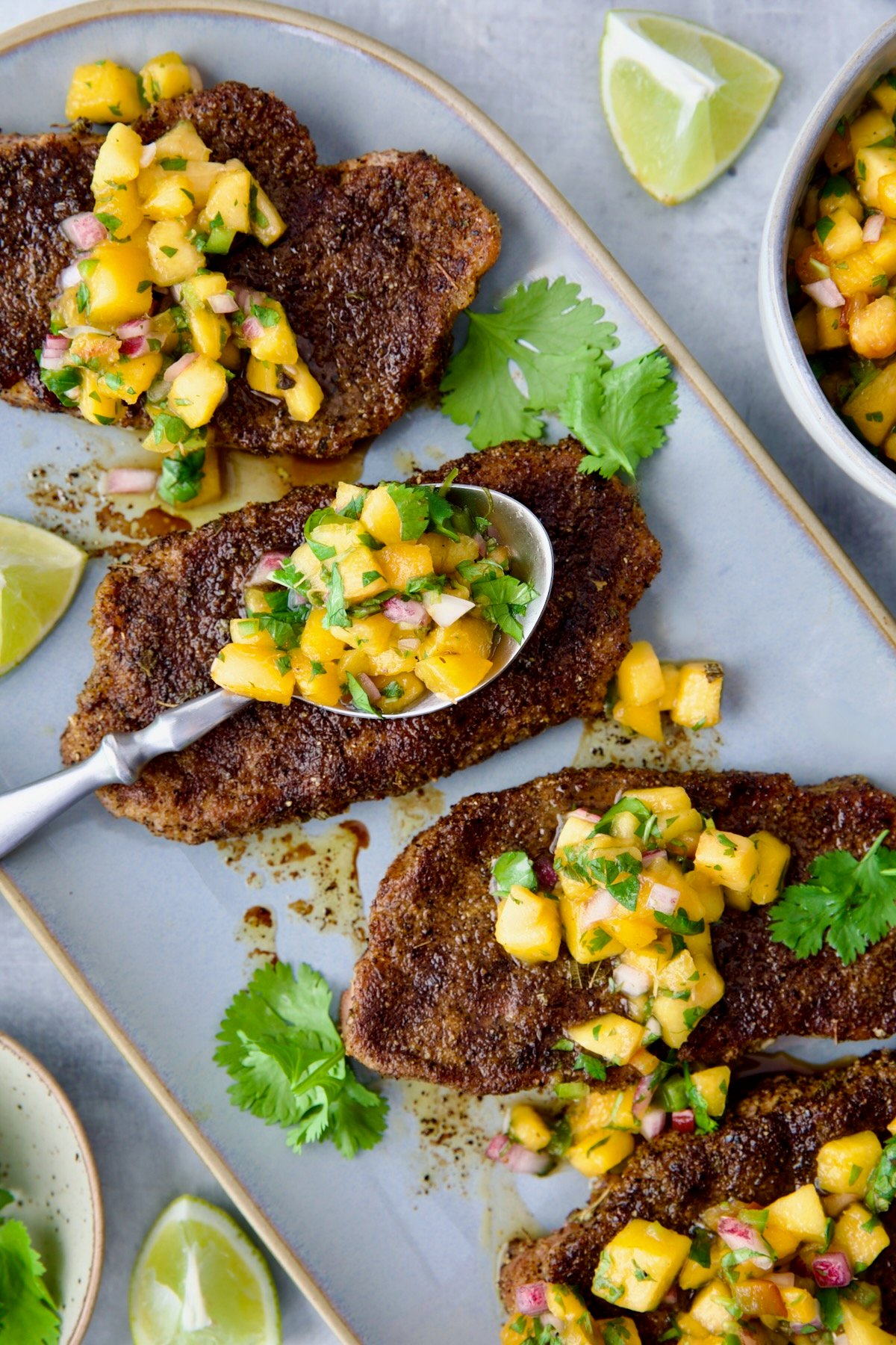 Four grilled Pork Chops with Peach Salsa on oval gray platter with salsa-filled spoon resting on one of the chops.