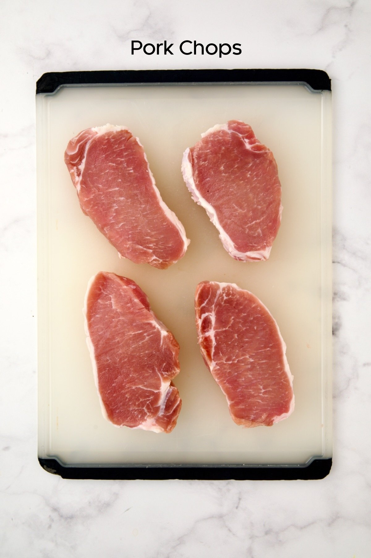 Four uncooked boneless pork chops on white plastic cutting board.