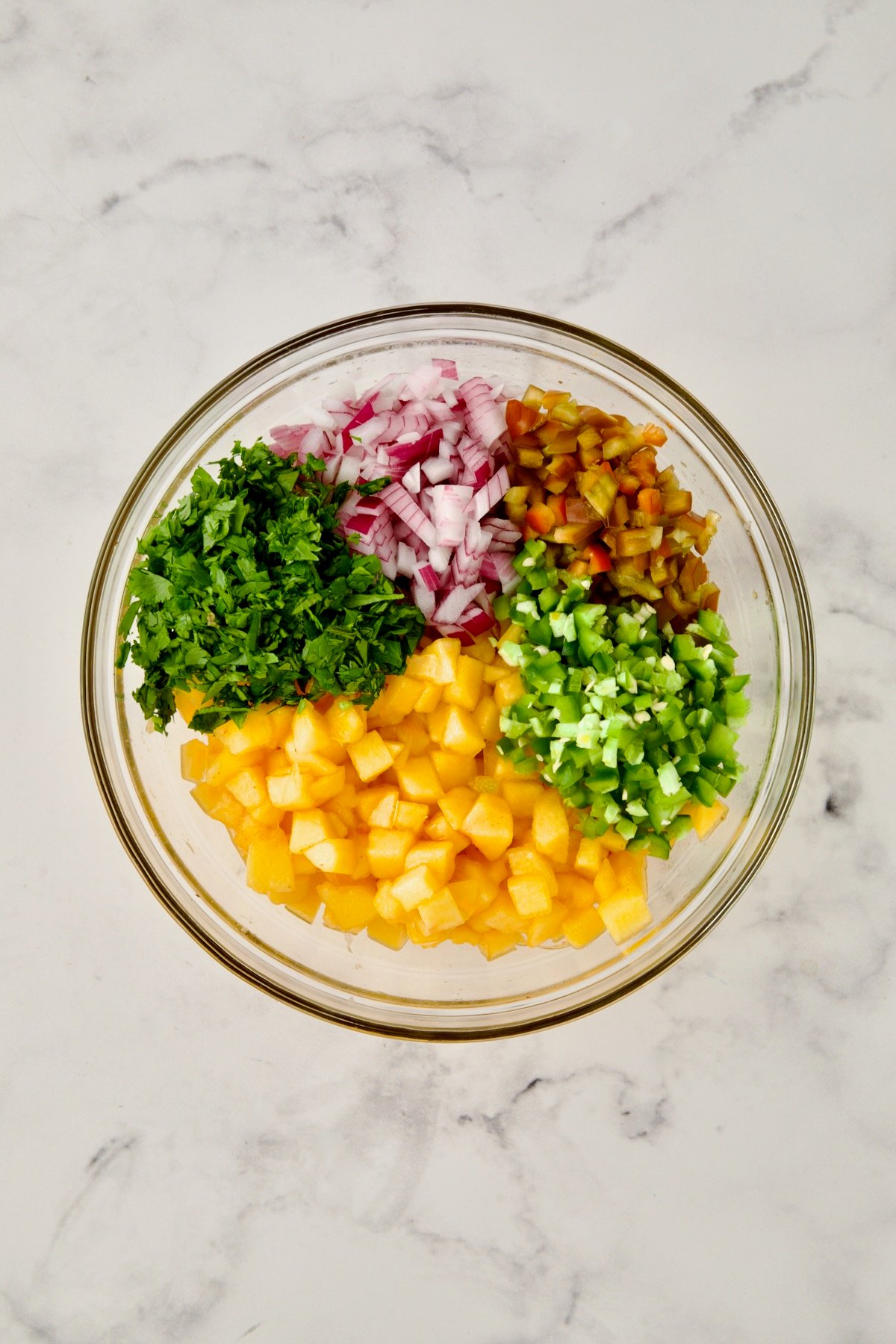 Ingredients for peach salsa in glass bowl before being stirred together.