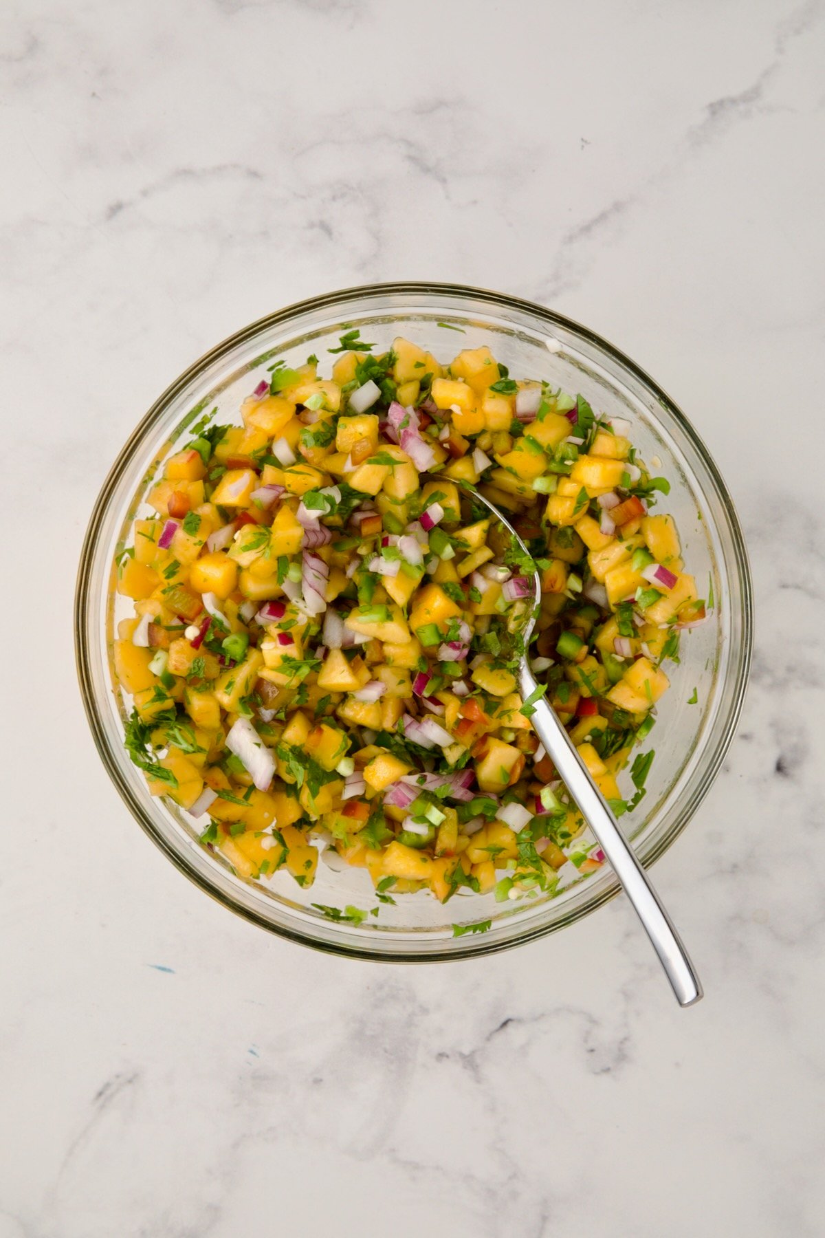 Ingredients for peach salsa in glass bowl before after stirred together.