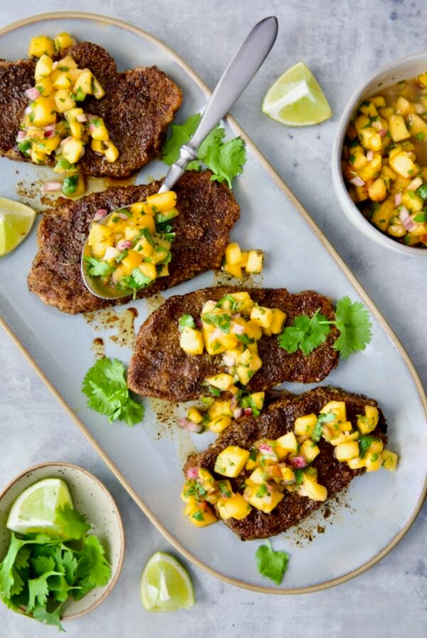 Four Pork Chops with Peach Salsa on oval gray platter with spoon placing some of the salsa on each pork chop.