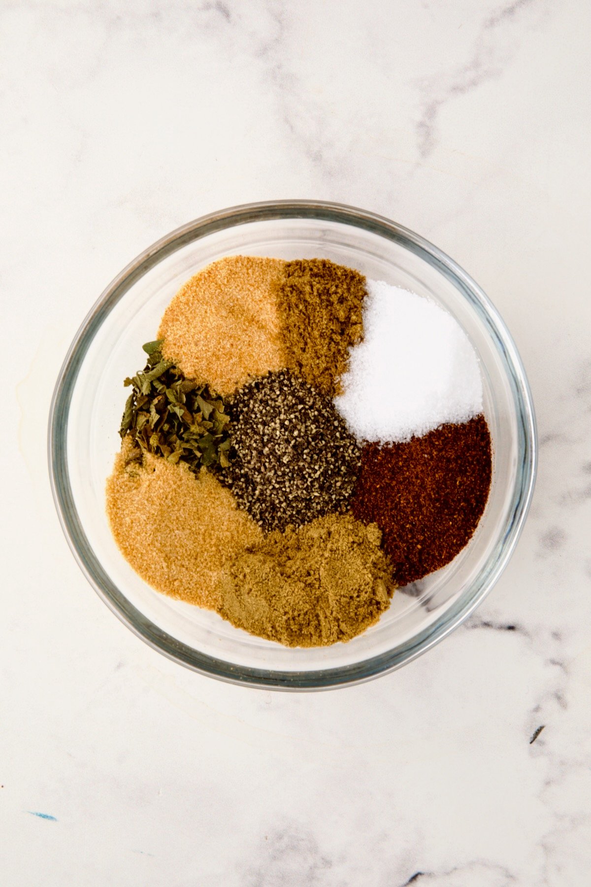 Spices for spice rub in glass bowl before being stirred together.