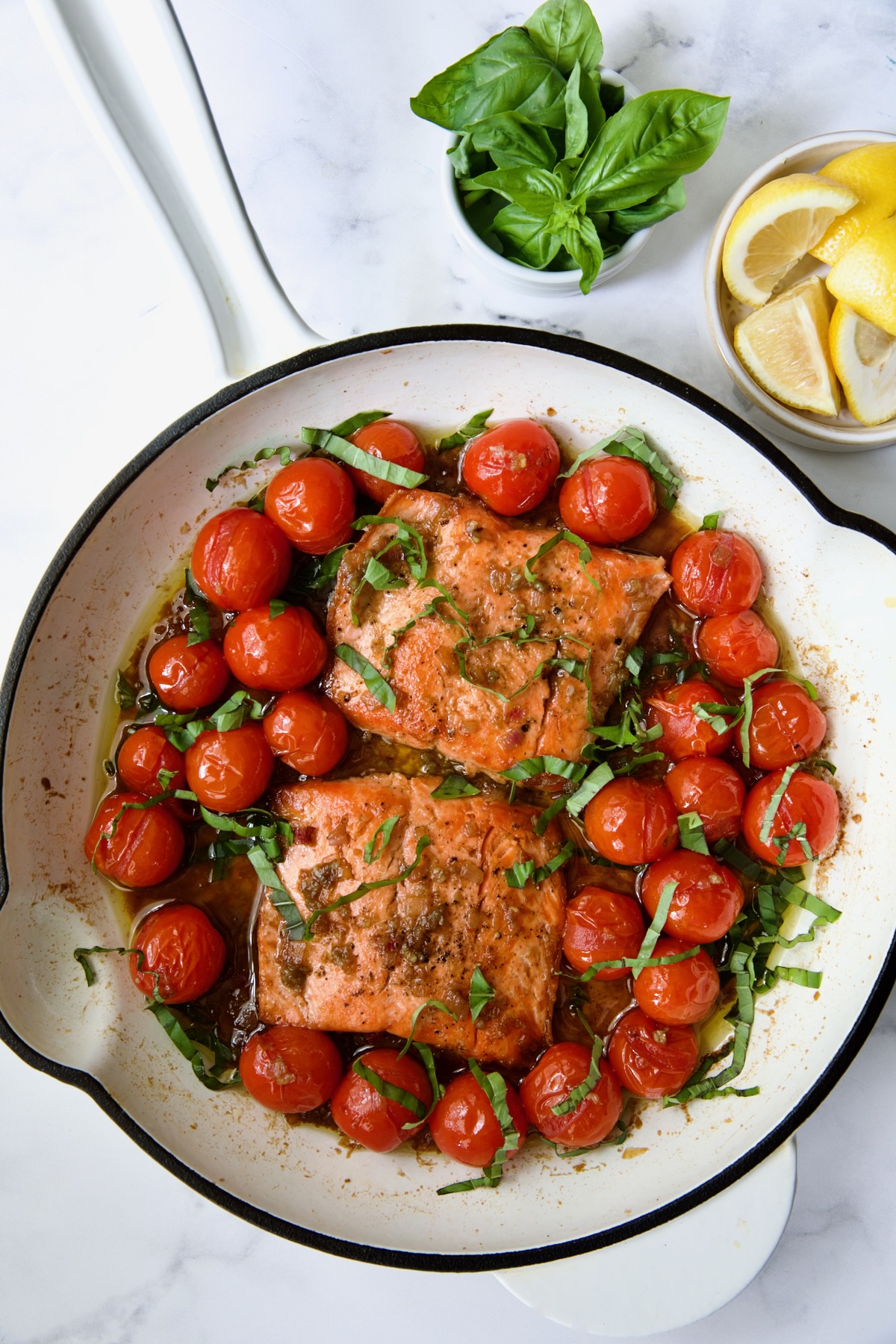 Finished Salmon with Balsamic Cherry Tomatoes in white enamel cast iron skillet with sliced basil added.