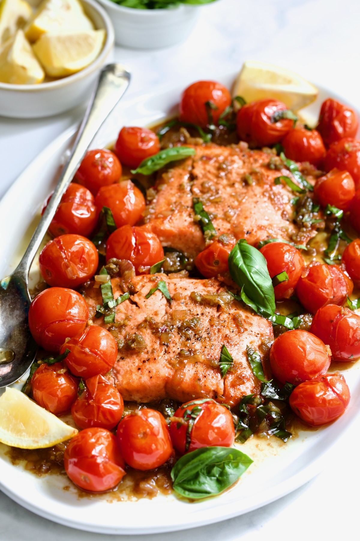 Salmon with Balsamic Cherry Tomatoes on oval white platter with serving fork garnished with lemon wedges.
