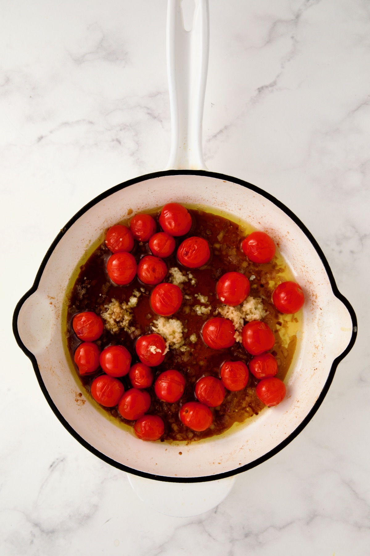 Balsamic vinegar added to shallots, tomatoes and garlic in white enamel cast iron skillet.