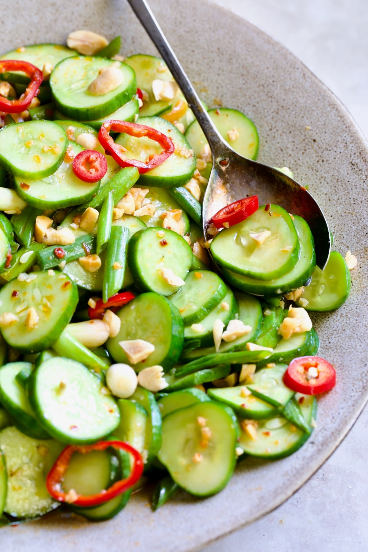 Spicy Asian Cucumber Salad in earthenware bowl with serving spoon garished with peanuts.