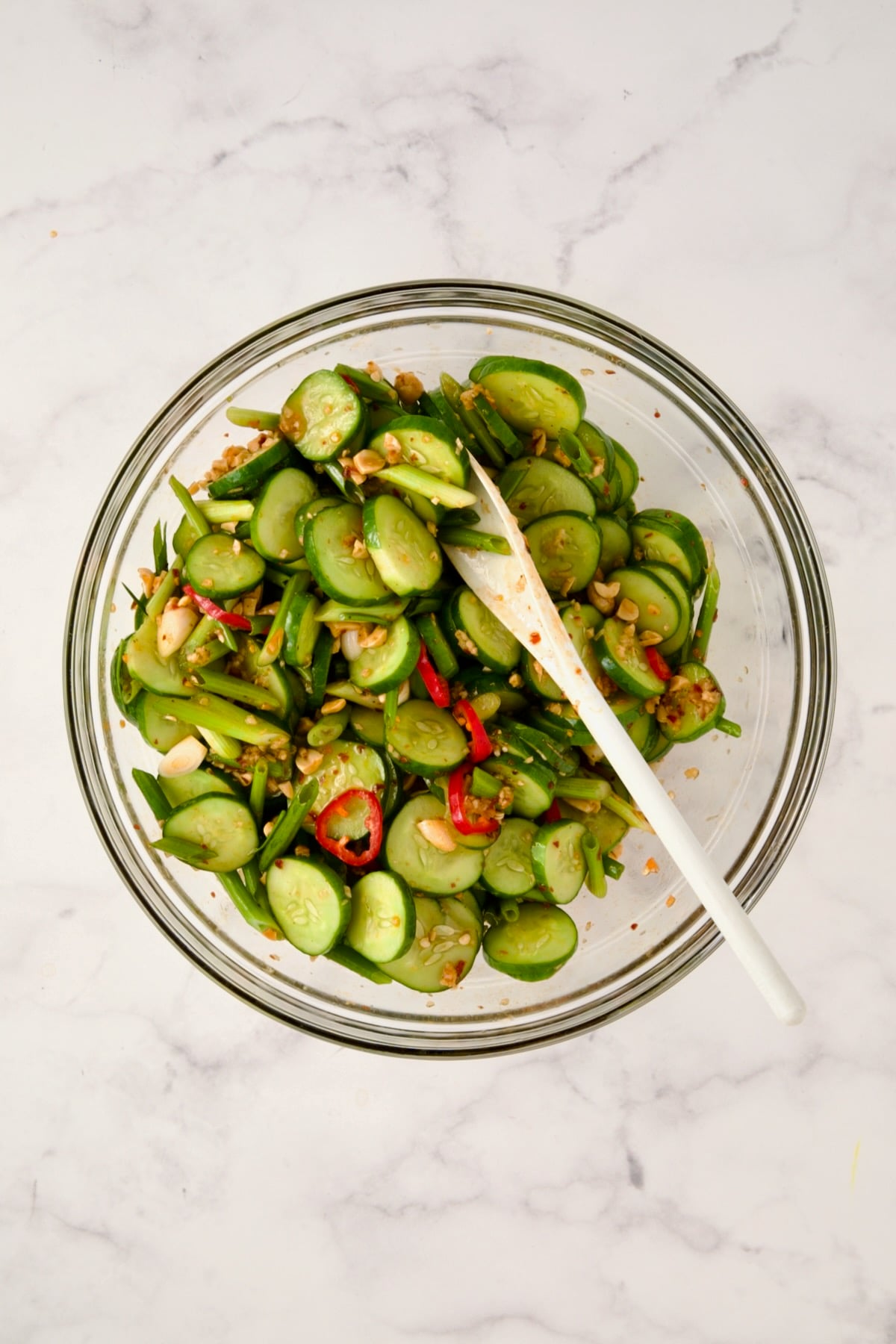 Spicy Asian Cucumber Salad being stirred together in glass bowl with white mixing spoon.