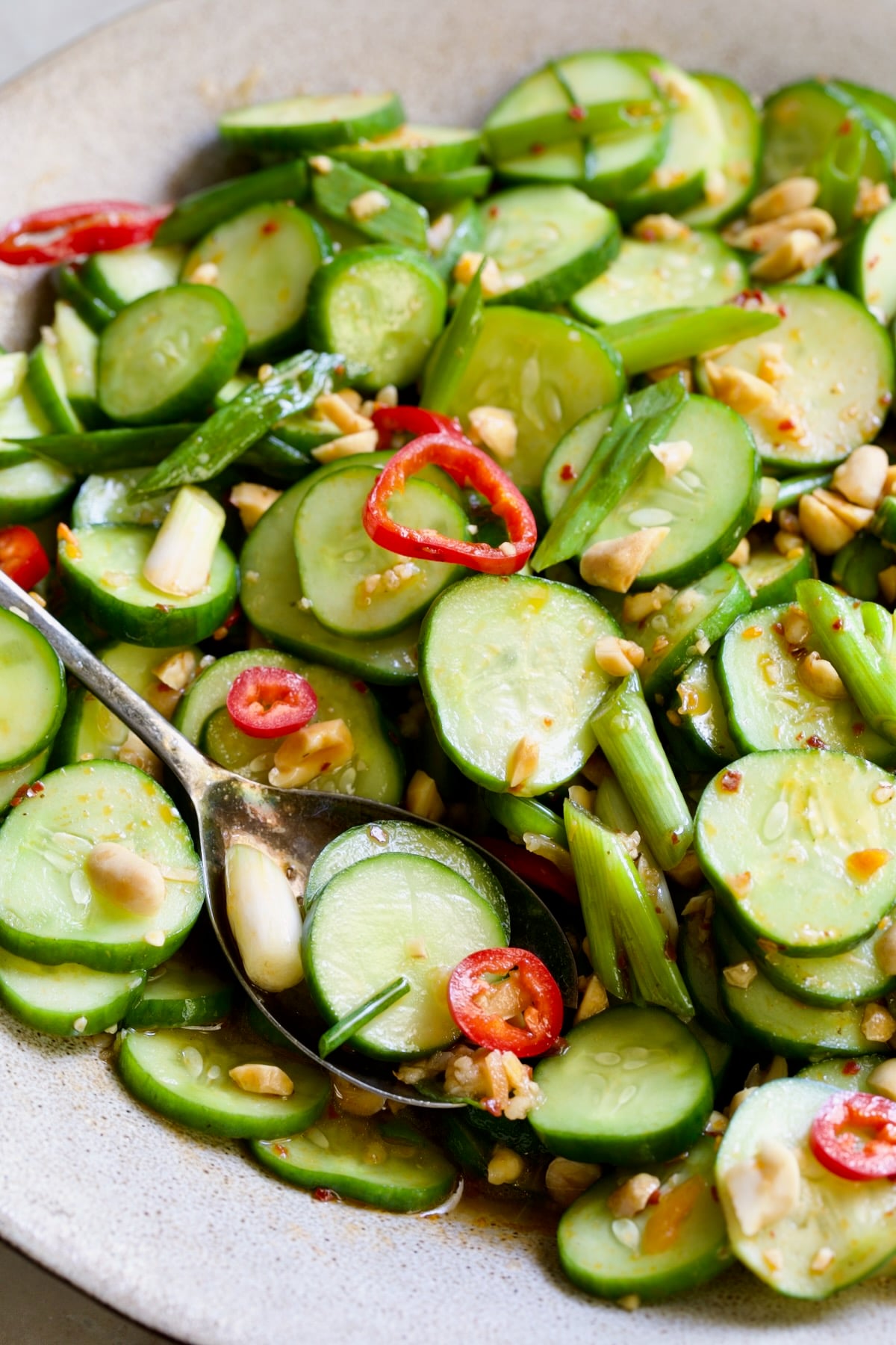 Spicy Asian Cucumber Salad in earthenware bowl with serving spoon garished with peanuts.
