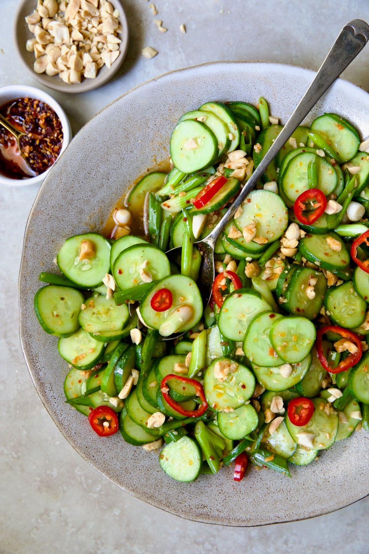 Spicy Asian Cucumber Salad in earthenware bowl with serving spoon garished with peanuts.