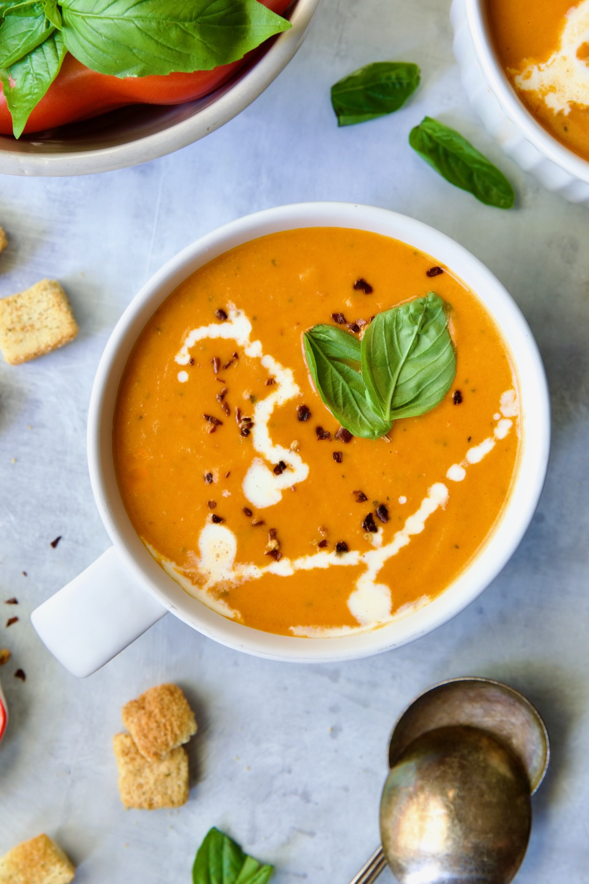 Creamy Tomato and Basil Soup in a white soup mug garnished with fresh basil leaves.