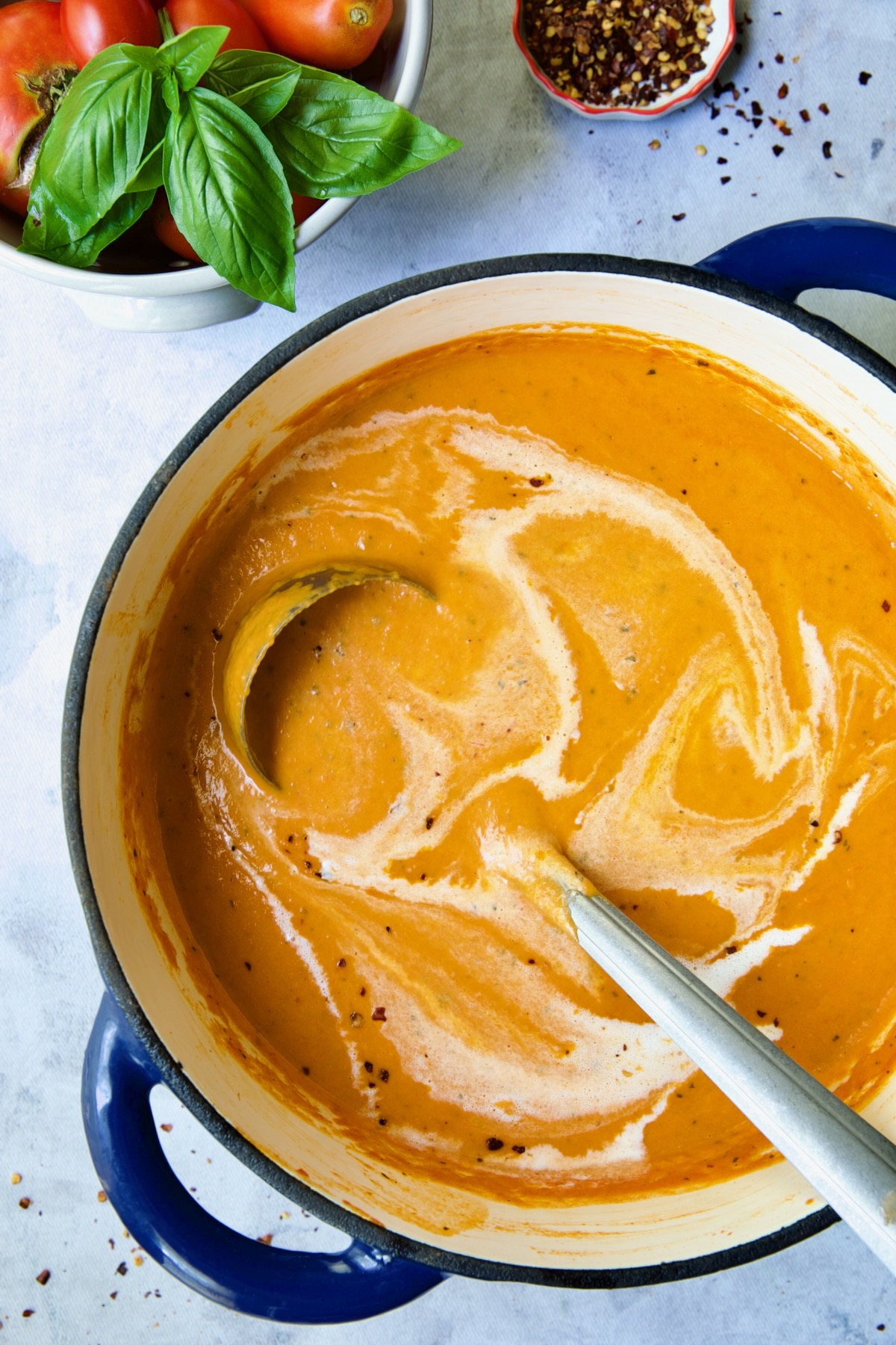 Creamy Tomato and Basil Soup in blue Dutch oven with more cream swirled in.