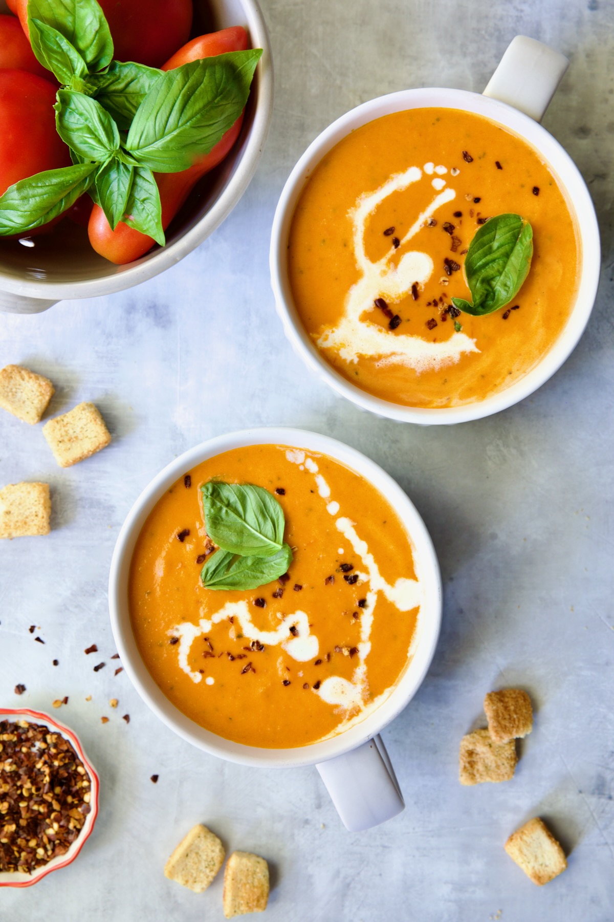 Two servings of Creamy Tomato and Basil Soup in white soup mugs.