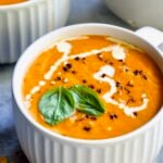 Creamy Tomato and Basil Soup in a white soup mug garnished with fresh basil leaves.