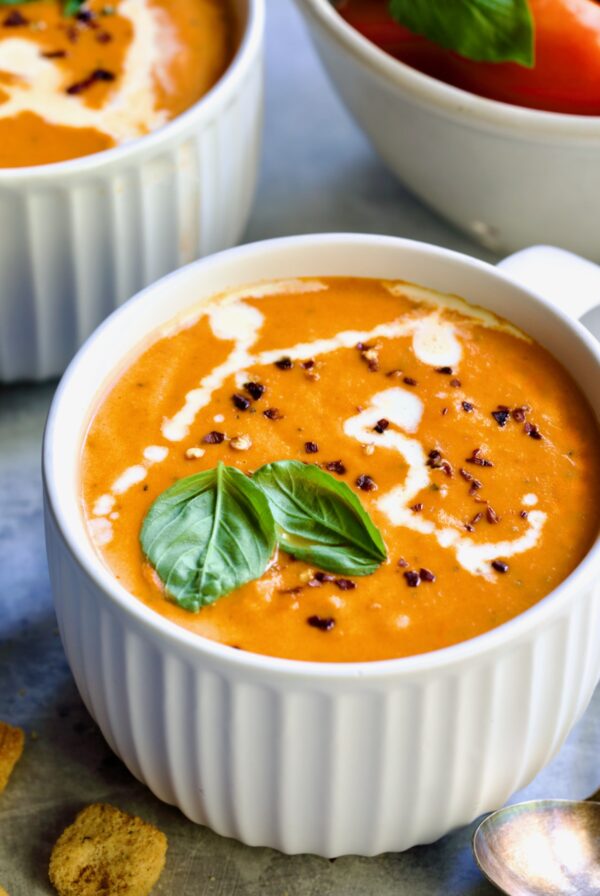 Creamy Tomato and Basil Soup in a white soup mug garnished with fresh basil leaves.