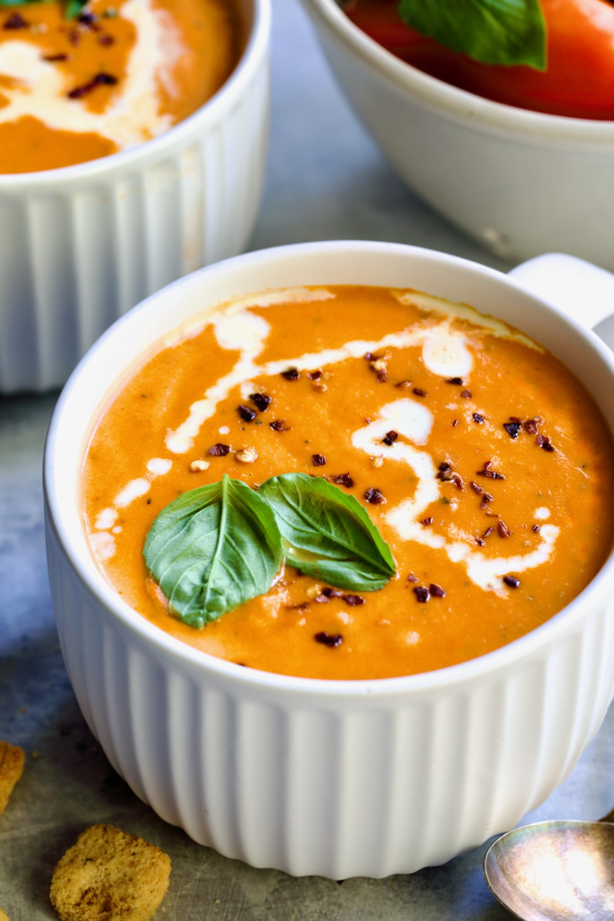 Creamy Tomato and Basil Soup in a white soup mug garnished with fresh basil leaves.
