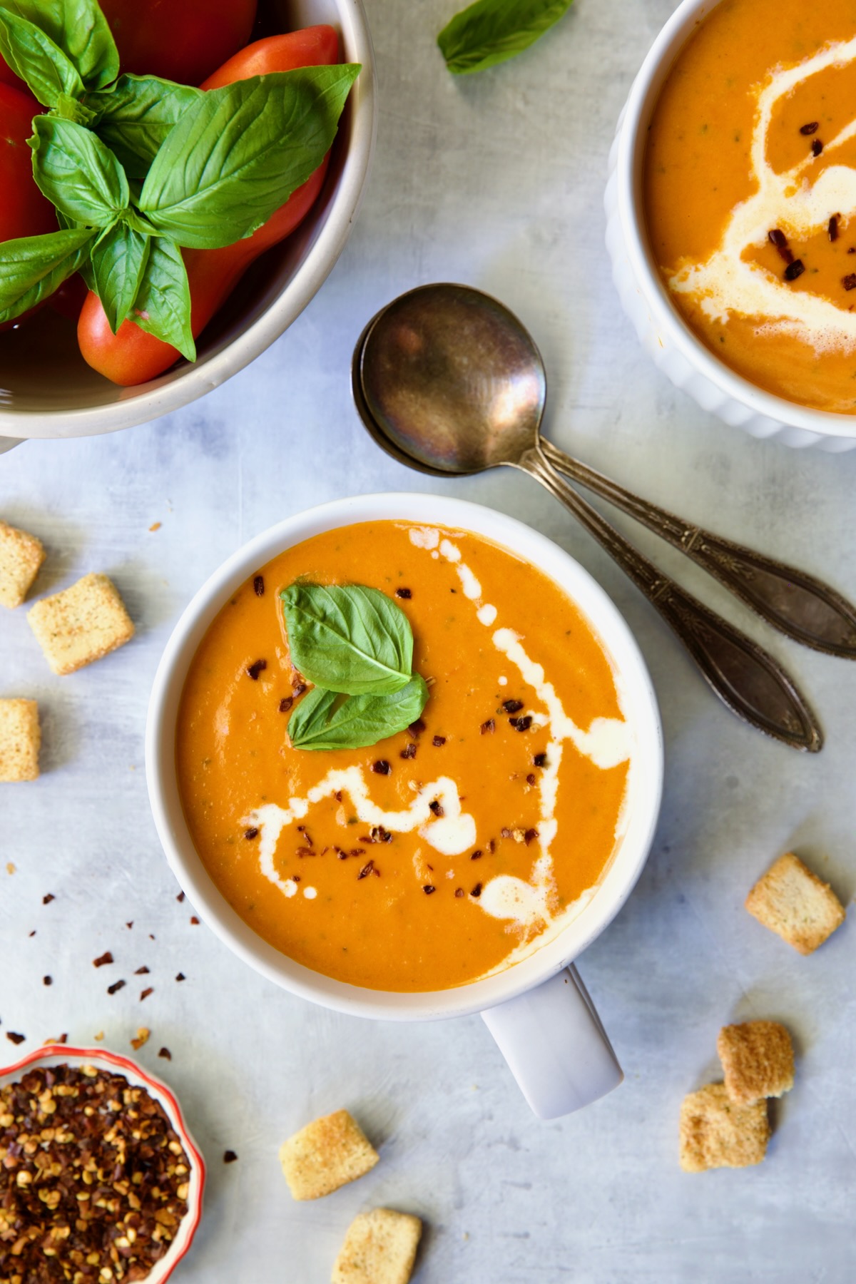 Two servings of Creamy Tomato and Basil Soup in white soup mugs garnished with fresh basil leaves.