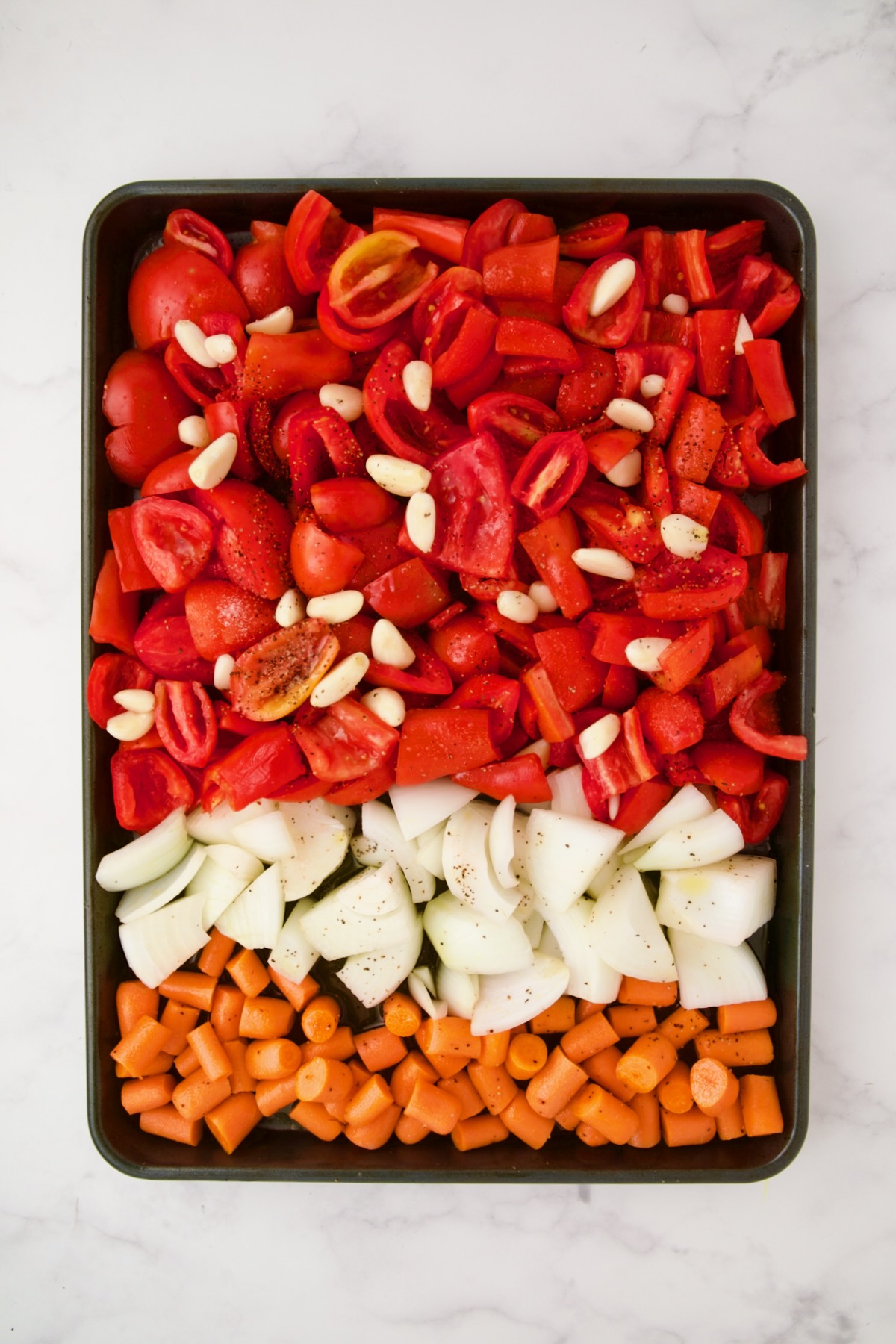 Chunks of tomatoes, onion, carrots and garlic on rimmed baking sheet before being roasted.