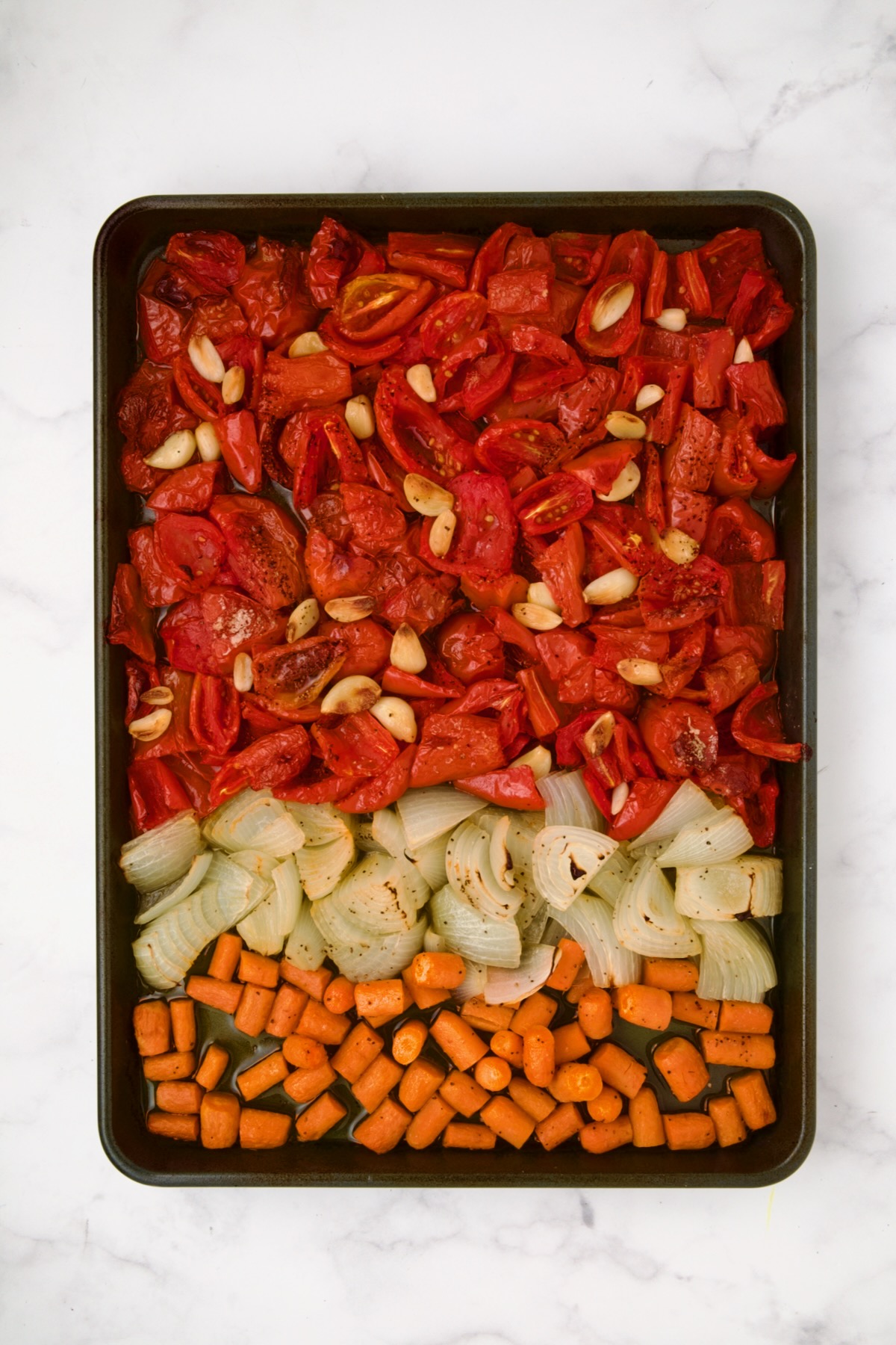 Chunks of tomatoes, onion, carrots and garlic on rimmed baking sheet after being roasted.