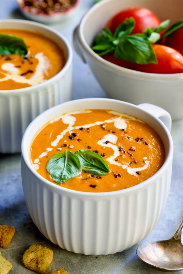 Creamy Tomato and Basil Soup in a white soup mug garnished with fresh basil leaves.