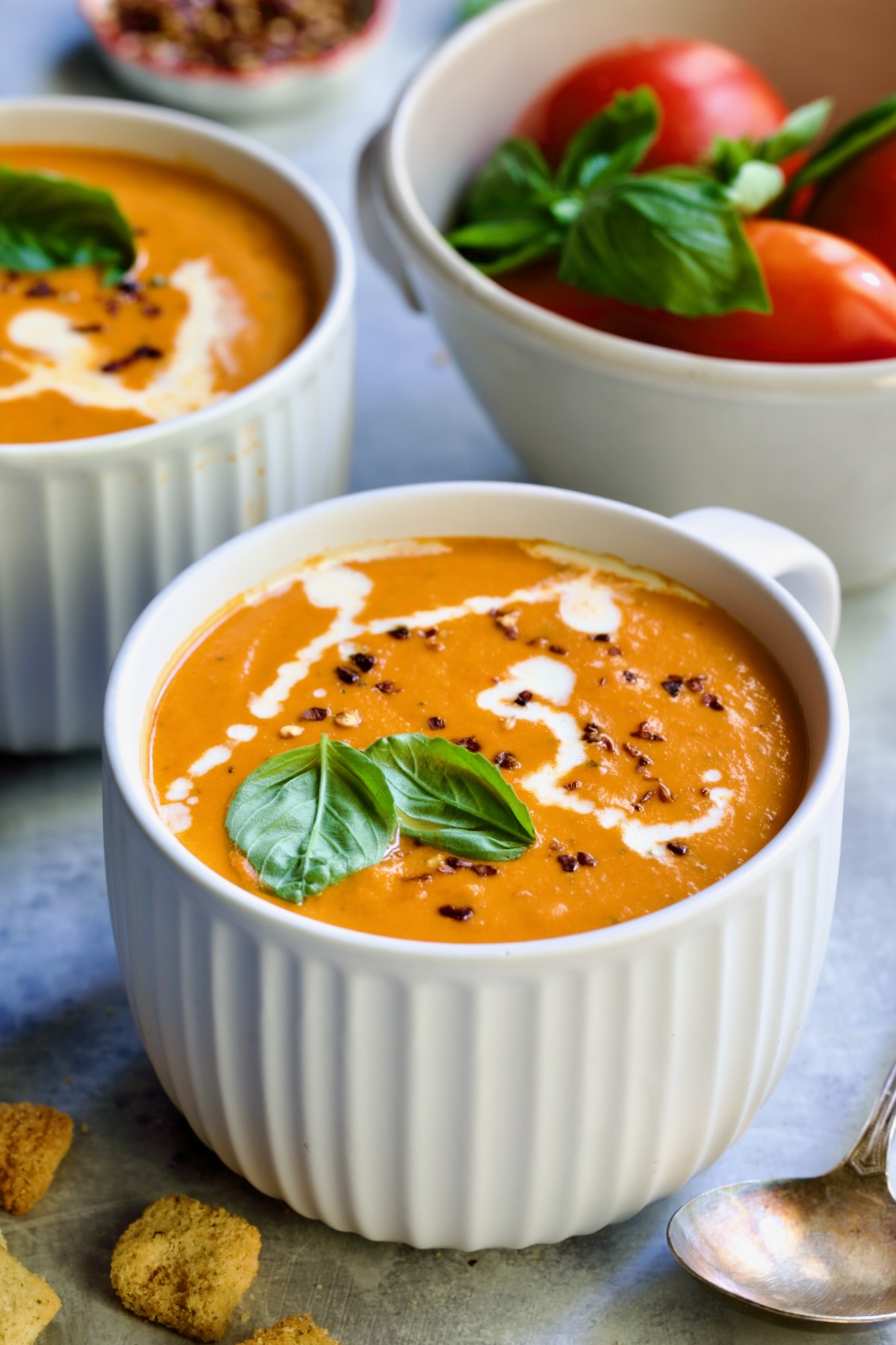 Creamy Tomato and Basil Soup in a white soup mug garnished with fresh basil leaves.