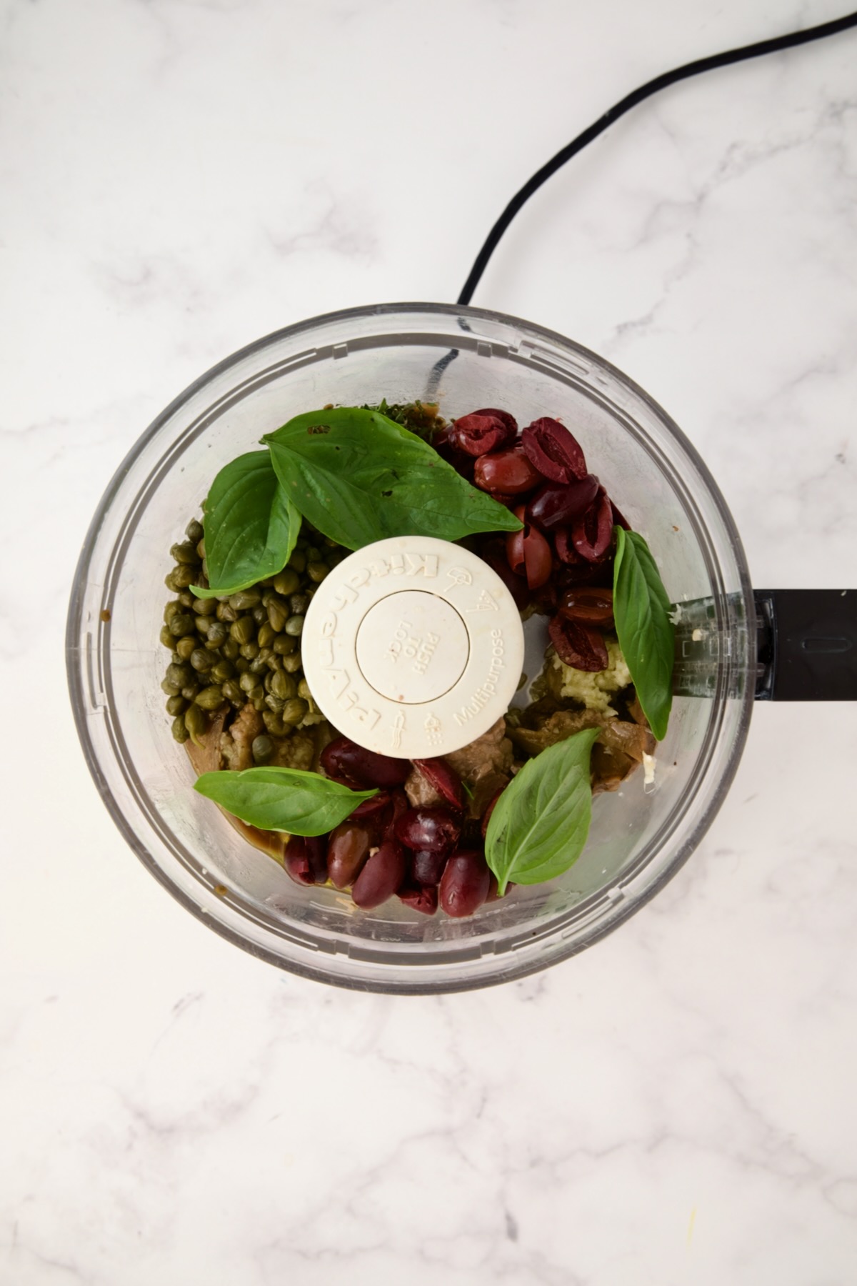 Cooked eggplant in food processor after other ingredients are added before being pureed.