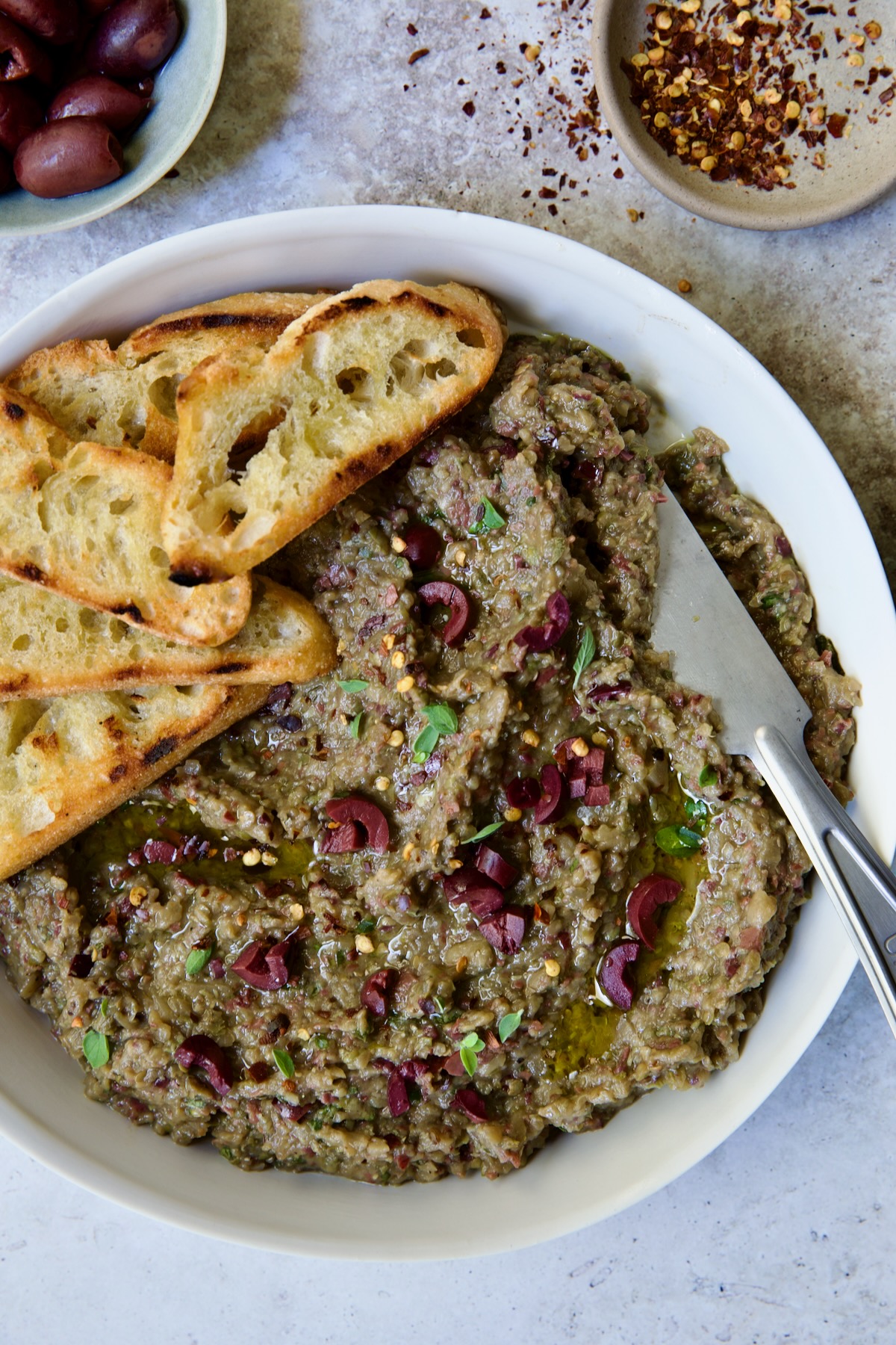 Eggplant Caviar (Caviar d'Aubergine) in white bowl with five pieces of grilled bread on the side with knife.