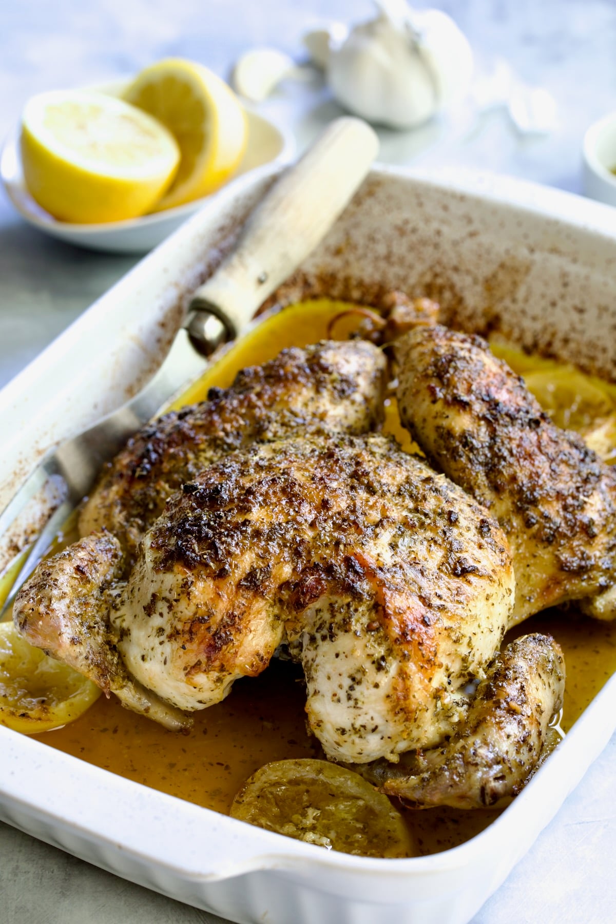 Greek Roast Chicken in white rectangular roasting pan with meat fork.