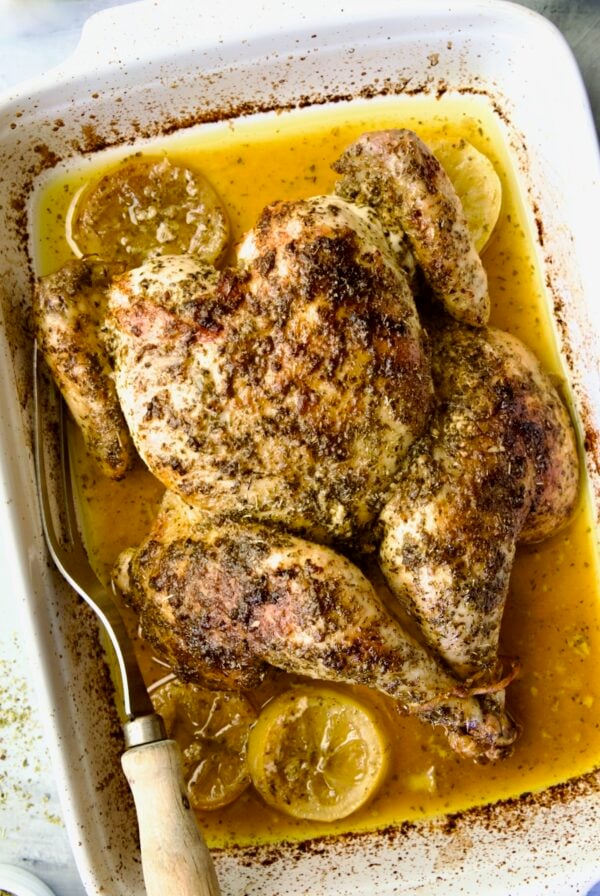 Greek Roast Chicken in white rectangular roasting pan with meat fork.