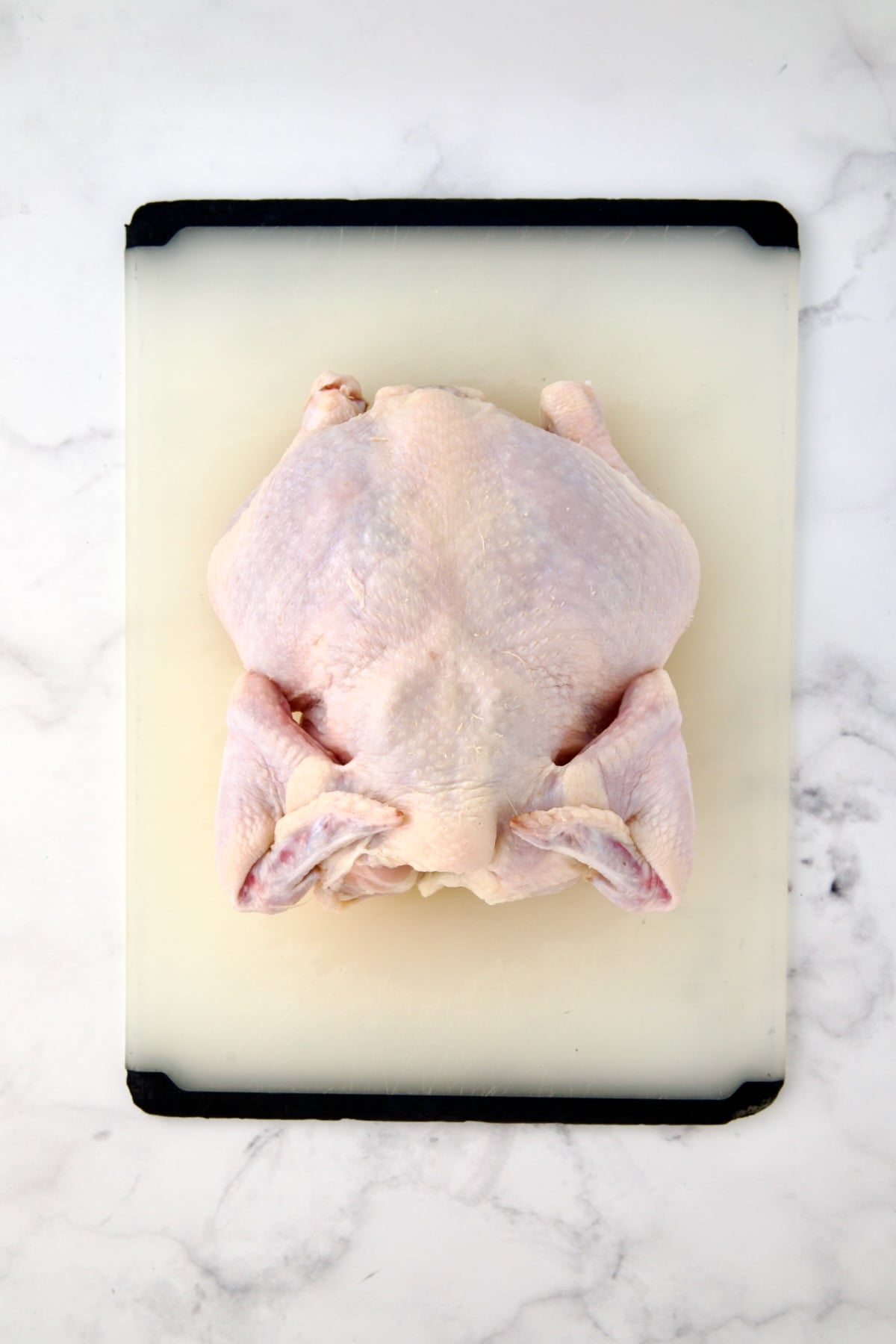 Fryer-size chicken breast side down on white plastic cutting board.