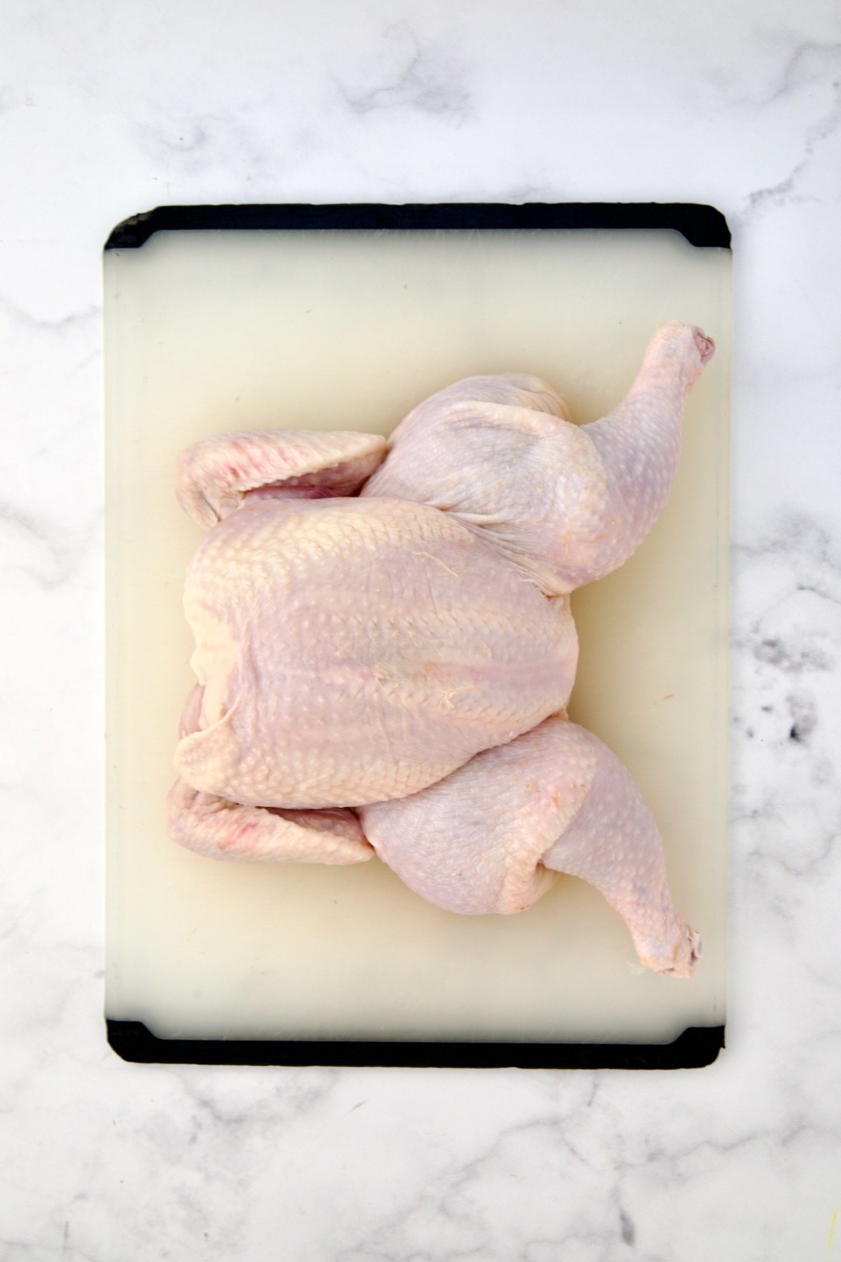 Spatchcocked fryer-size chicken on white plastic cutting board.
