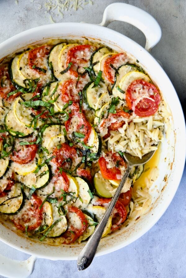 Orzo Vegetable Tian in round white baking dish with serving spoon.