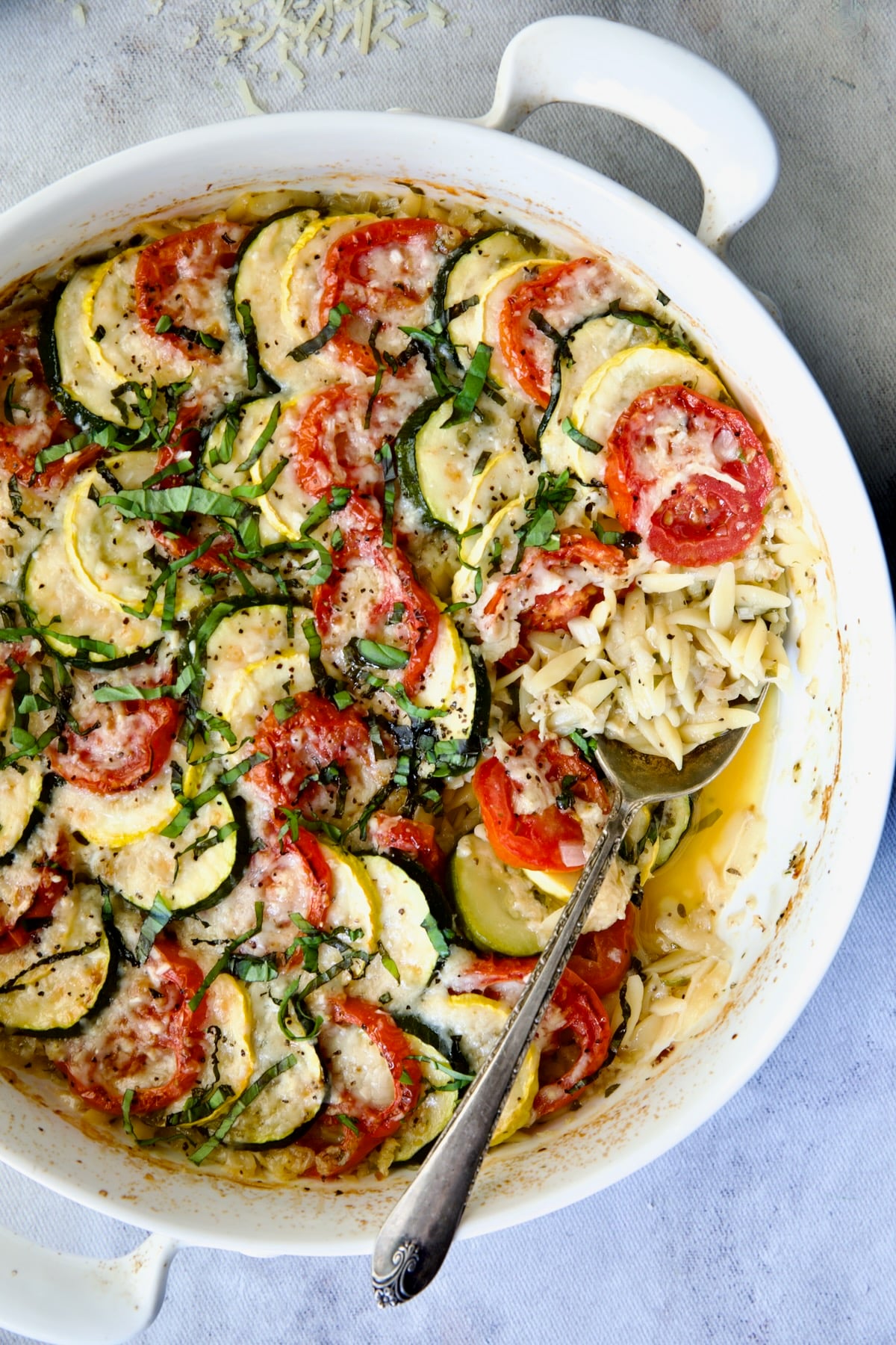 Orzo Vegetable Tian in round white baking dish with serving spoon.