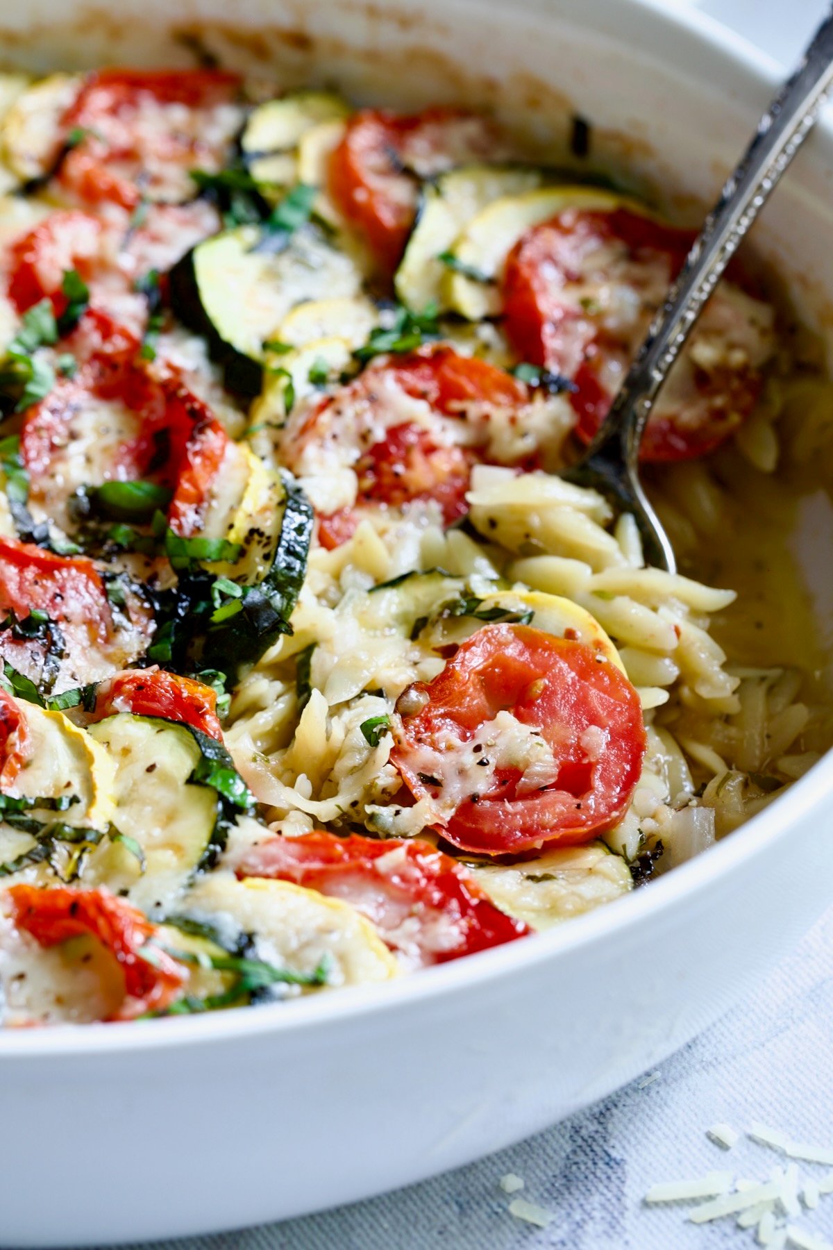 Orzo Vegetable Tian in round white baking dish with serving spoon.