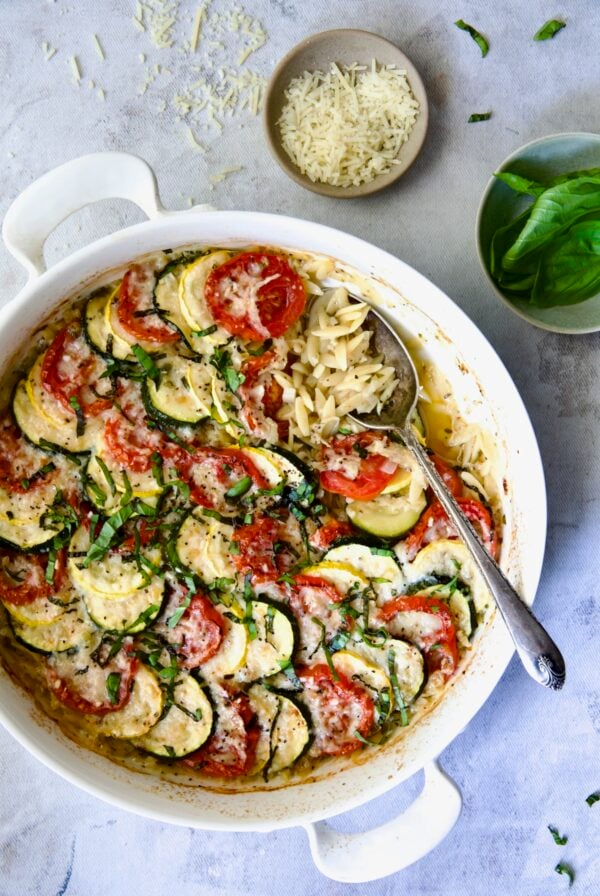 Orzo Vegetable Tian in round white baking dish with serving spoon.