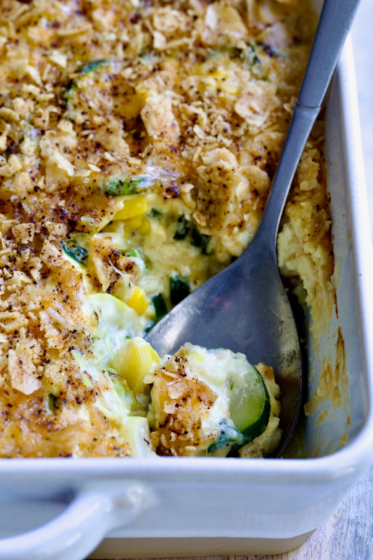 Summer Squash Corn Poblano Casserole in rectangular white baking dish with serving spoon.