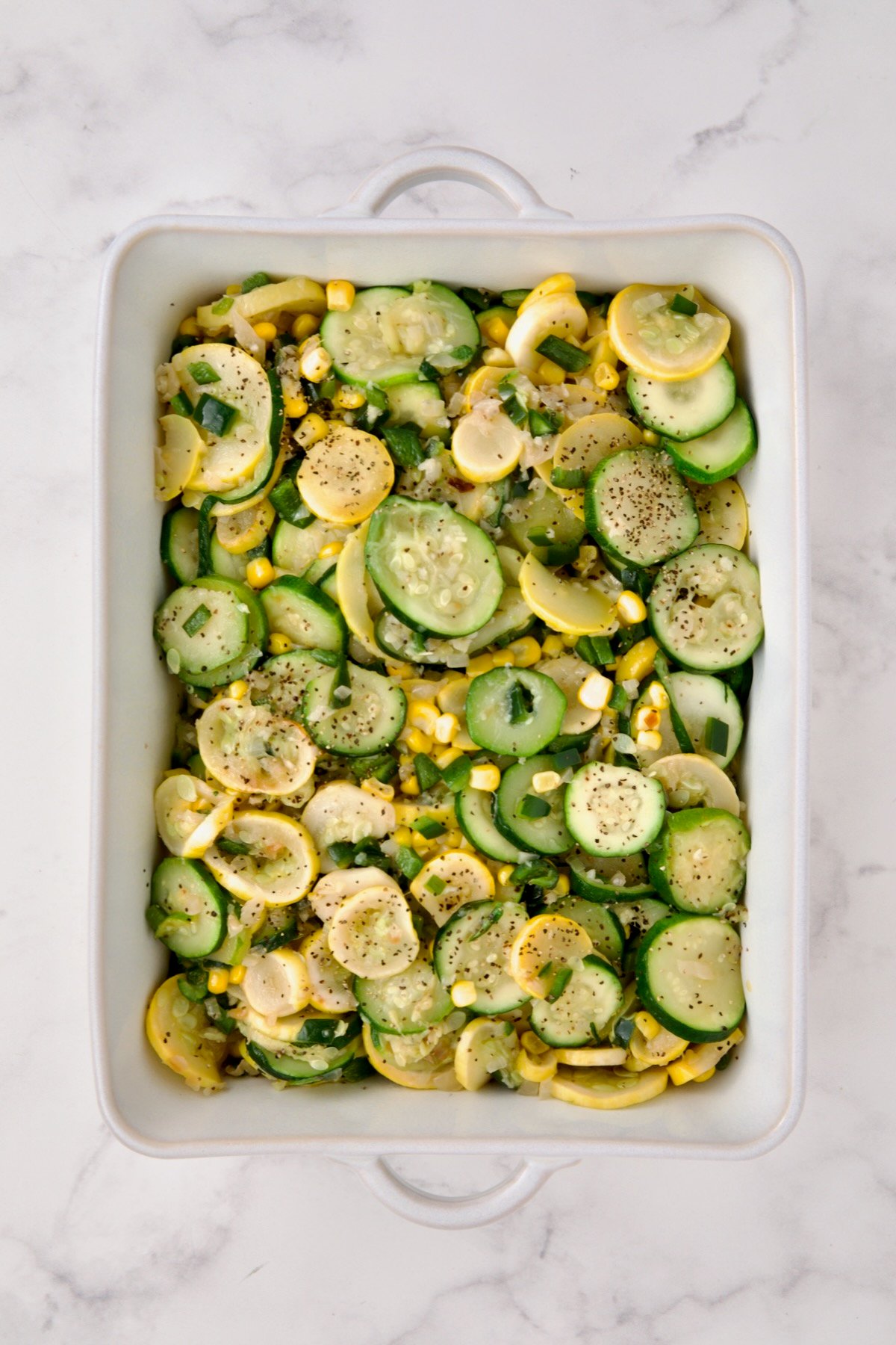 Cooked zucchini, yellow squash, poblano, and corn in white rectangular baking dish.