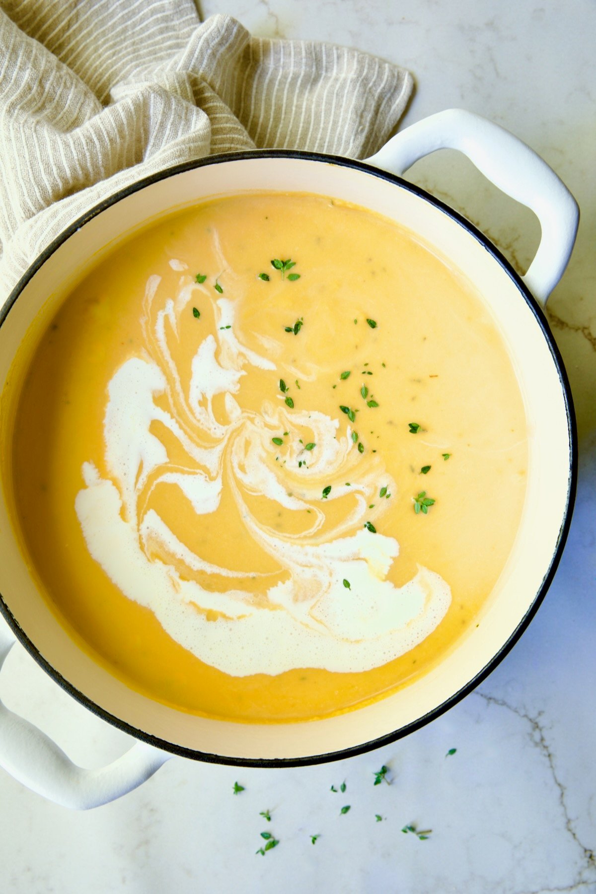 Butternut Squash Brie Soup in white enamel Dutch oven with a little extra cream and fresh thyme added for garnish.
