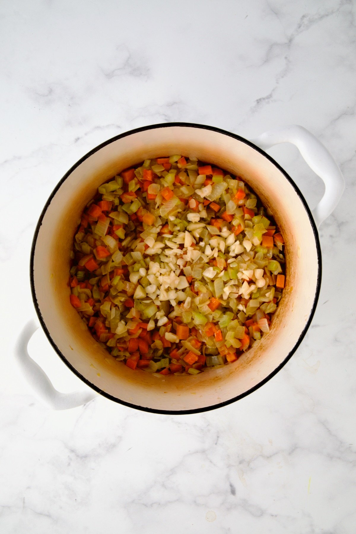 Garlic added to onions, carrots and celery in white enamel Dutch oven.