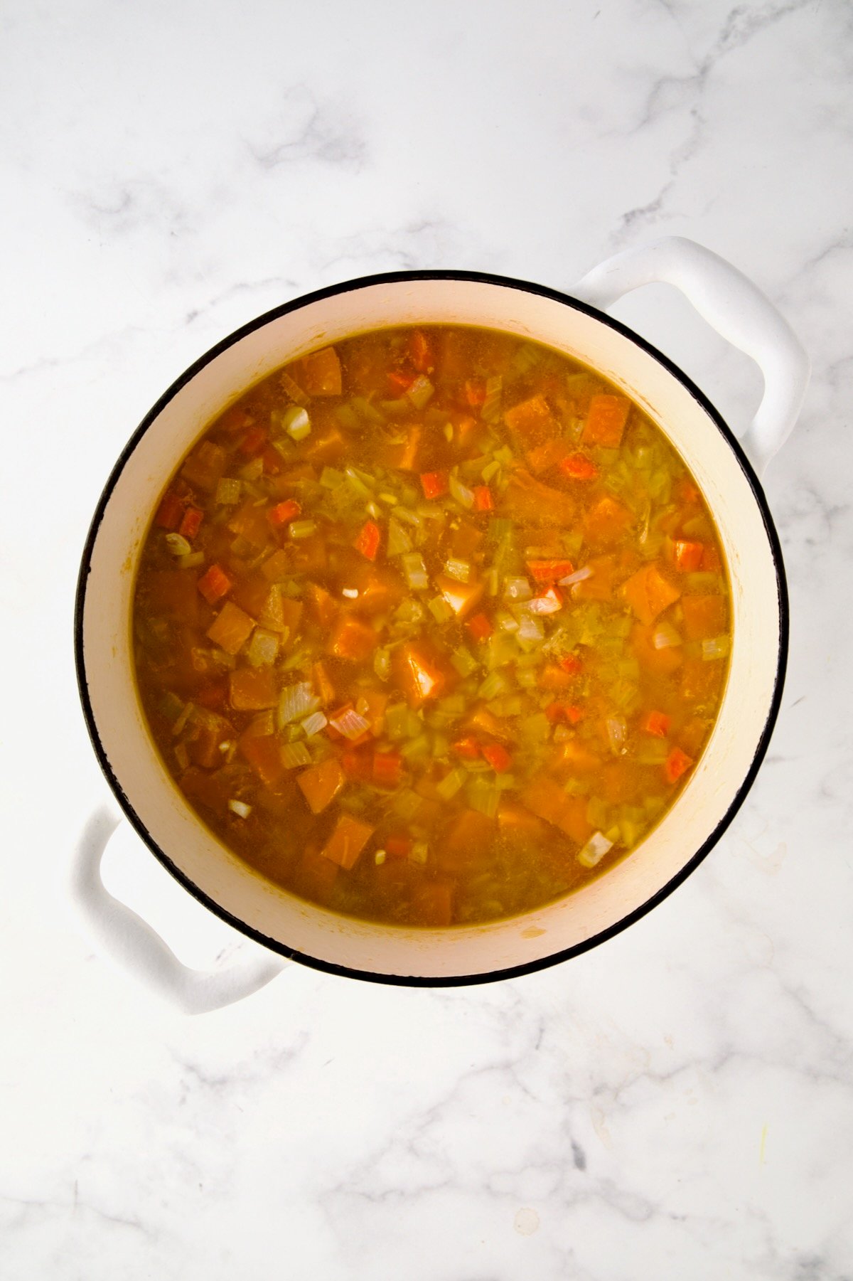 Cooked vegetables in broth in white enamel Dutch oven.