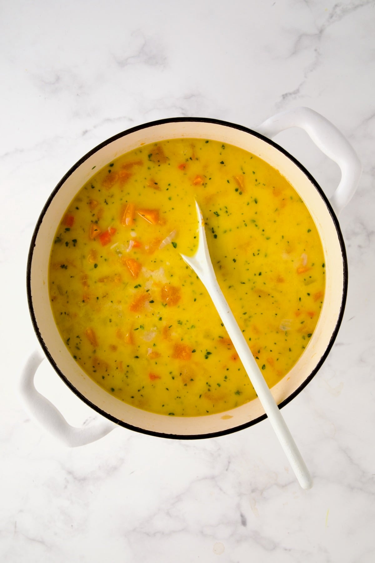 Brie, cream and chopped fresh thyme added to vegetables and broth in white enamel cast iron skillet stirred together.