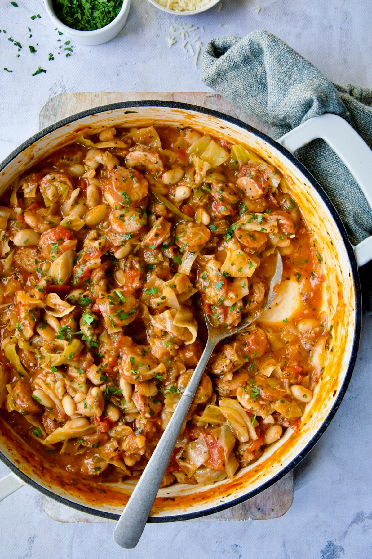 Cabbage Sausage White Bean Skillet in a white enamel cast iron pan with a serving spoon.