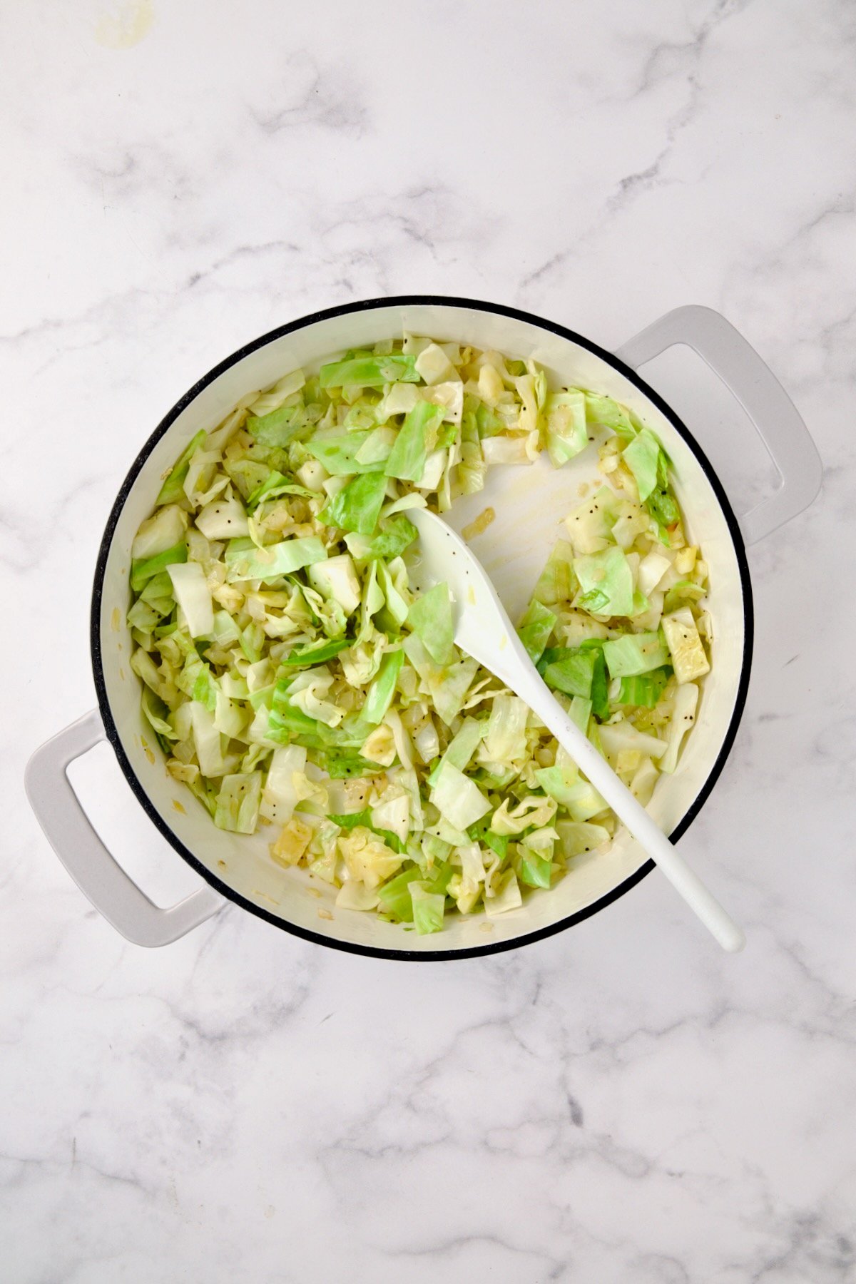 Cabbage being sauteed in white enamel cast iron skillet with onions.