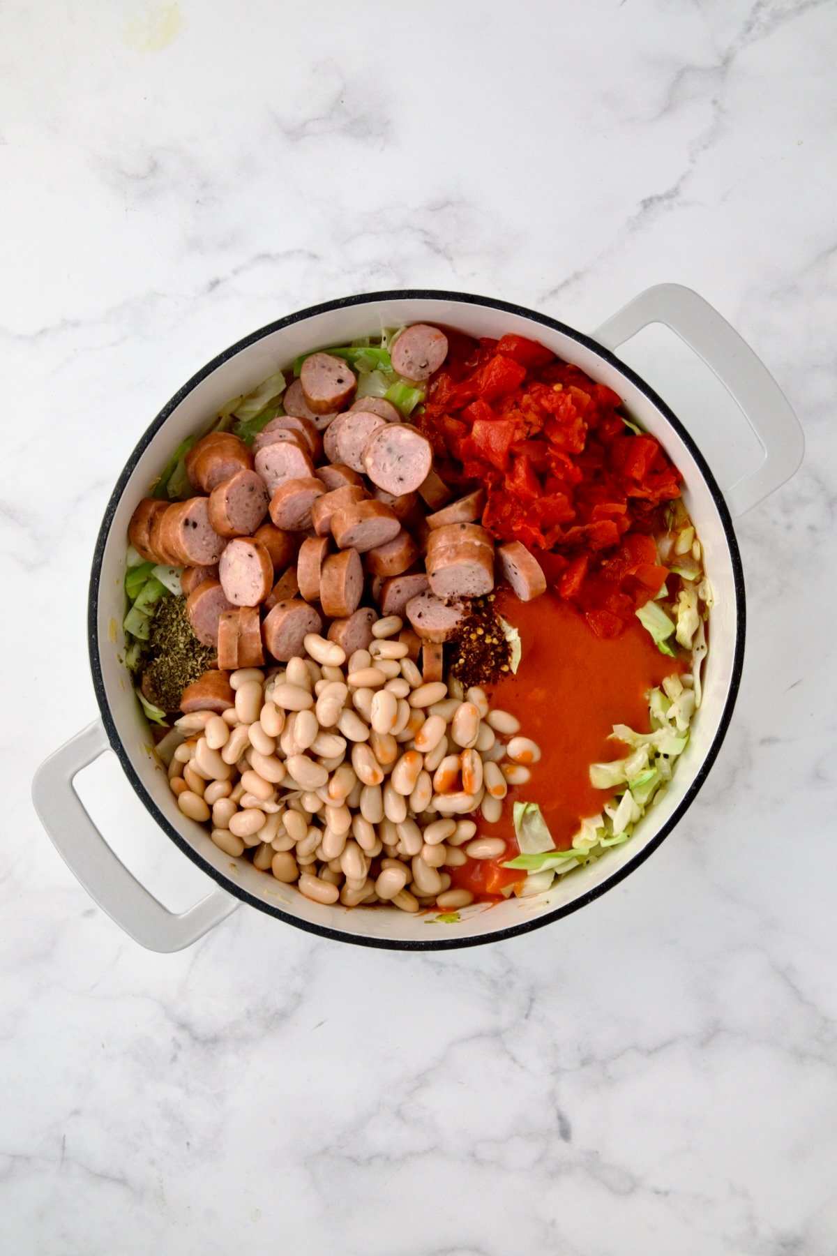 Sausage, beans, tomatoes, tomato soup, Italian seasoning, crushed red pepper flakes added to cabbage and onions in white enamel cast iron skillet.