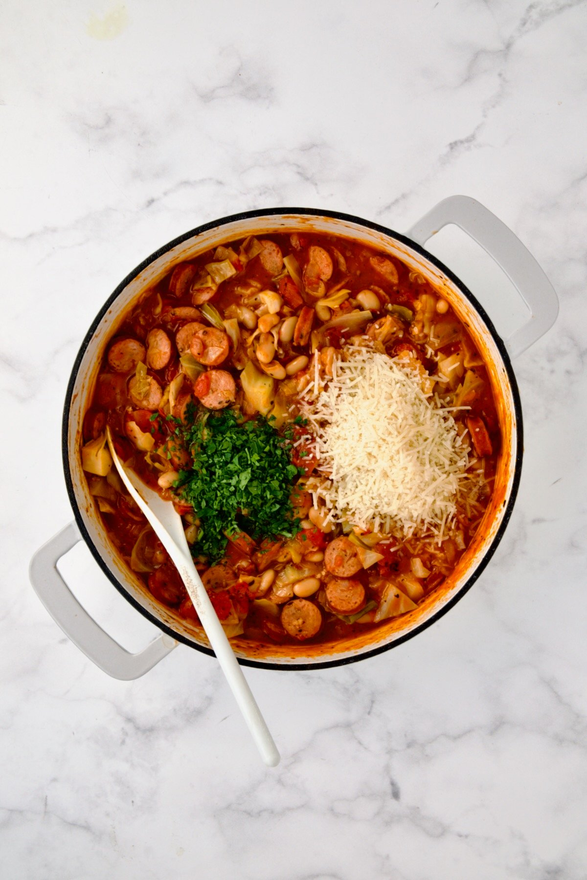 Parsley and cheese added to ingredients in white enamel cast iron skillet.