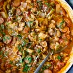 Cabbage Sausage White Bean Skillet in a white enamel cast iron pan with a serving spoon.