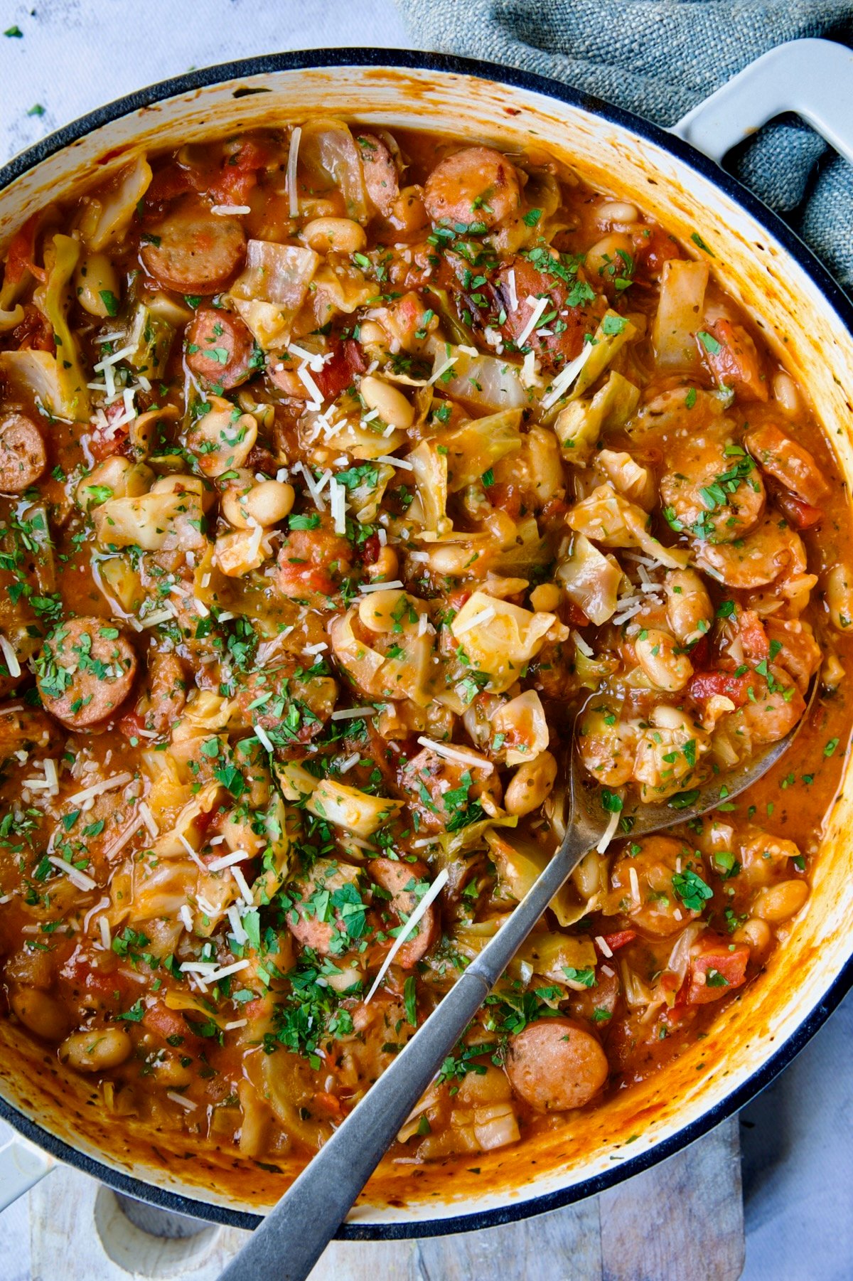 Cabbage Sausage White Bean Skillet in a white enamel cast iron pan with a serving spoon.