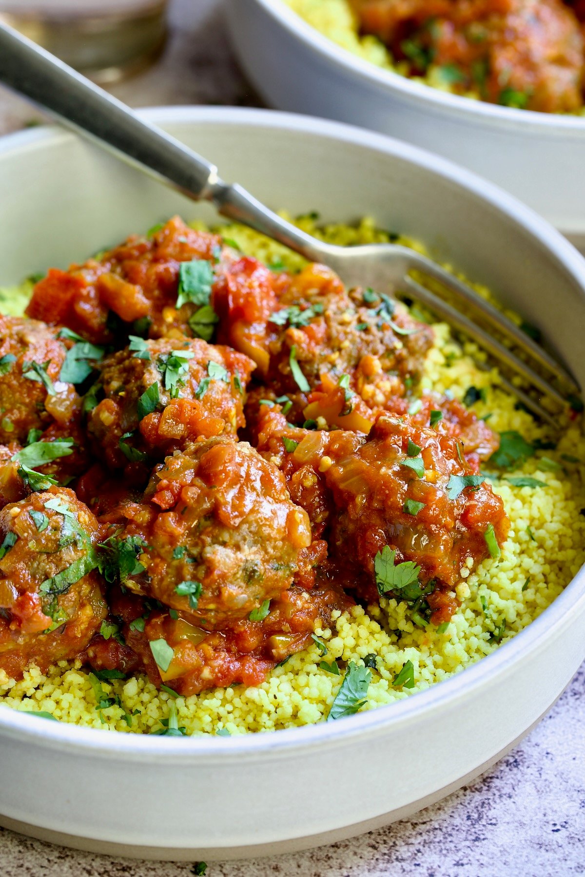 One serving of Moroccan Meatball Stew in earthenware bowl over couscous.
