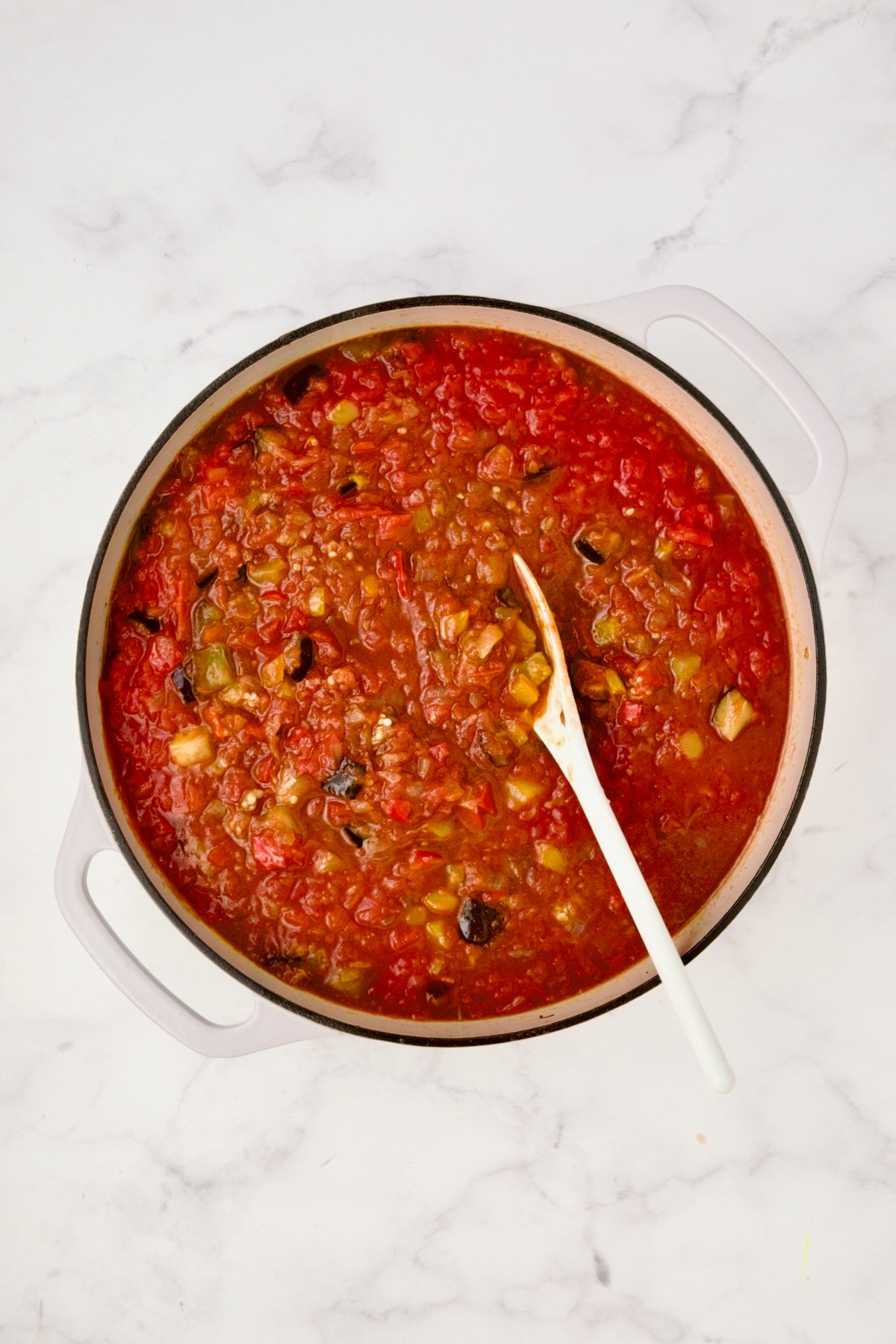 Crushed tomatoes and beef broth added to vegetables in white enamel cast iron skillet.