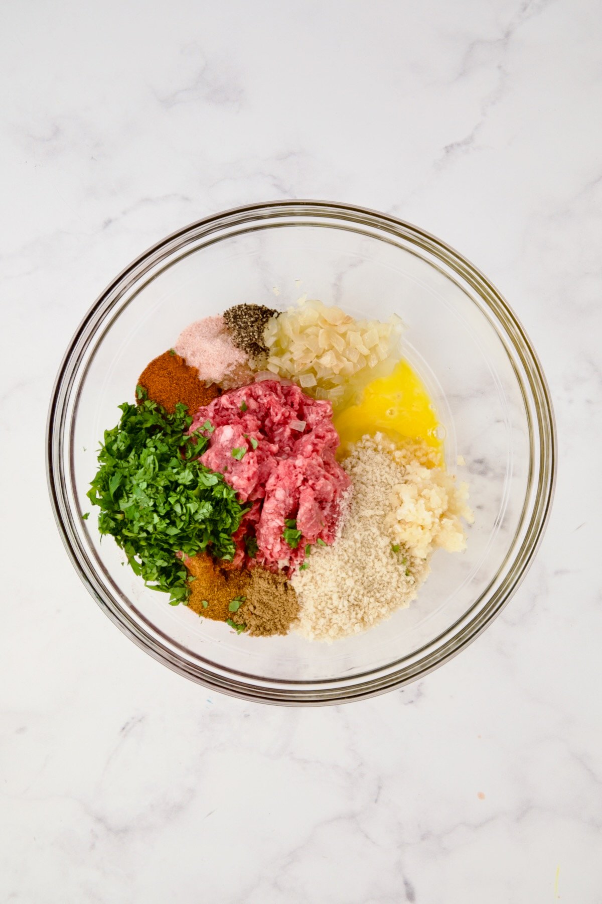 Ingredients for meatballs in glass bowl before being mixed together.